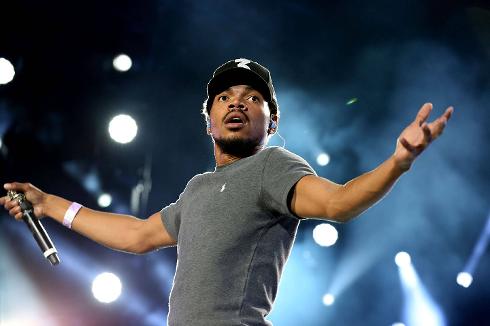 Chance the Rapper張開雙臂 壁紙 — 一位男歌手在明亮的聚光燈和藍色煙霧下張開雙臂，充滿活力地在舞台上表演。