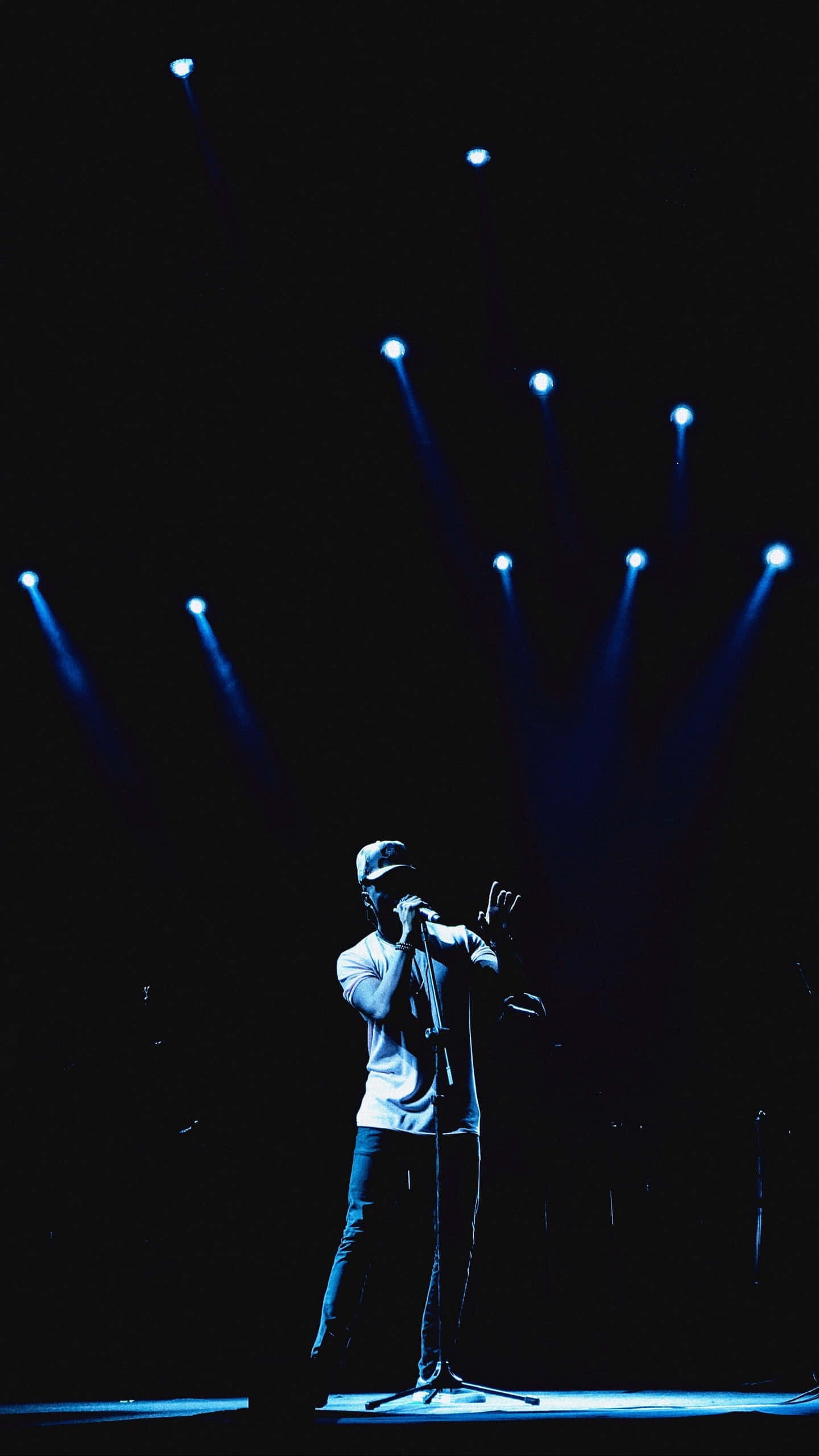 Chance The Rapper 演唱會舞台背景 壁紙 — 一位歌手在黑暗背景下，於戲劇性的藍色舞台燈光下表演。