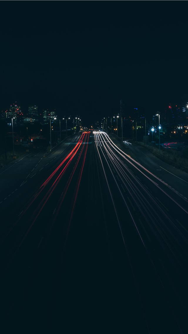 空曠高速公路 iPhone 深色背景 壁紙 — 長時間曝光捕捉到紅色和白色汽車燈光在夜間黑暗的城市高速公路上飛馳而過的光軌。