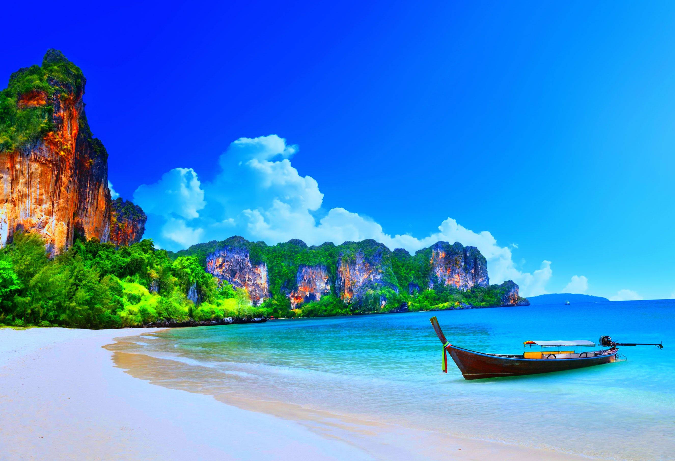 島嶼與海洋自然風景 壁紙 — 一艘長尾船停泊在碧綠色的海面上，旁邊是白色沙灘，四周被茂密的綠色懸崖環繞，上方是湛藍的天空。