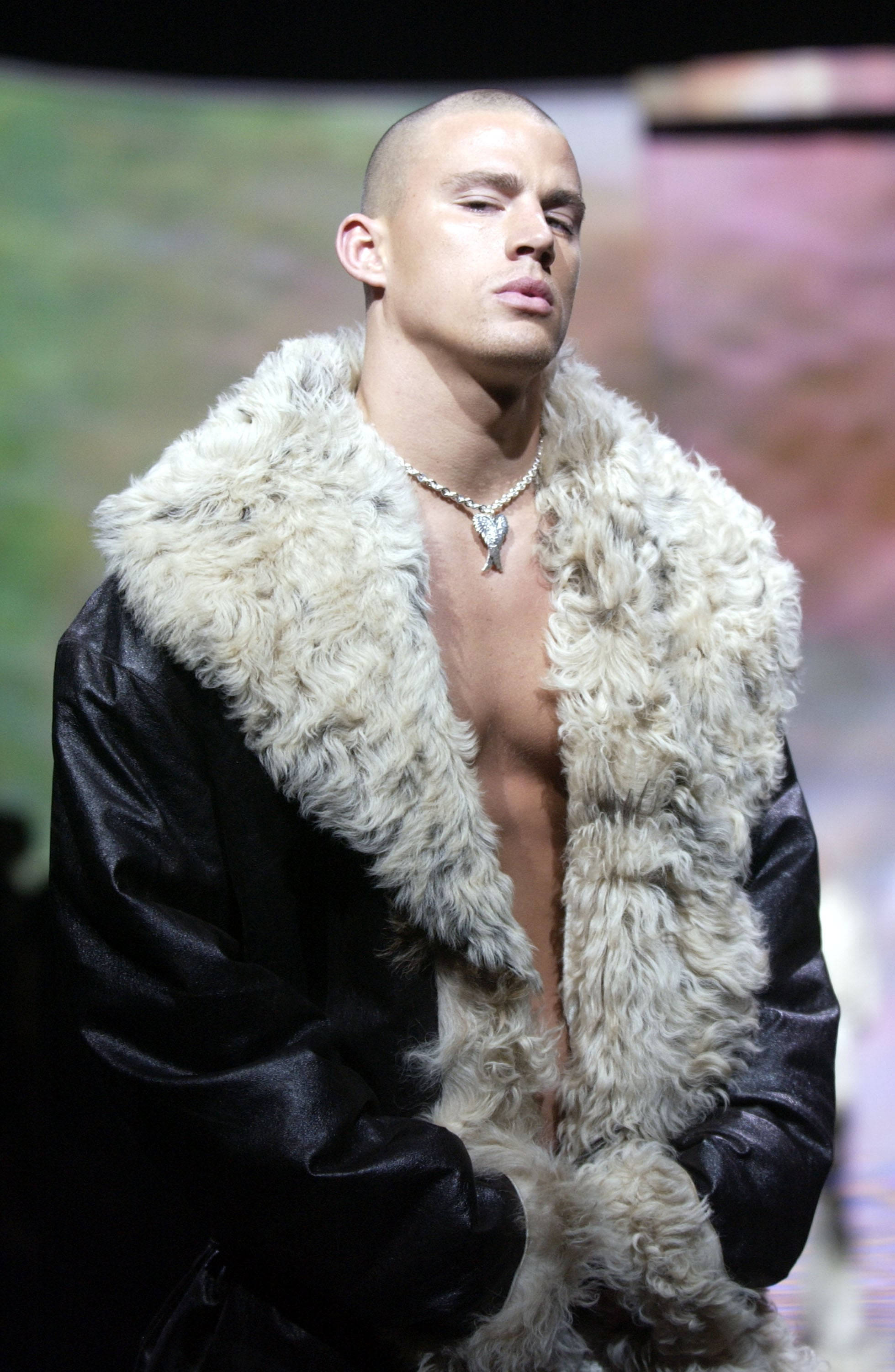 年輕時的 Channing Tatum 走秀造型 壁紙 — 一個光頭男人穿著黑色皮褸，配以白色蓬鬆毛領，在明亮燈光下自信地站在天橋上。