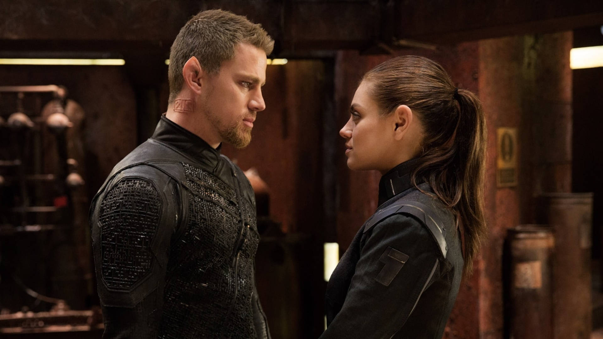 Channing Tatum 與 Mila Kunis 在《Jupiter Ascending》中的精彩對戲 壁紙 — 兩名身穿戰術裝備的特工在光線昏暗的工業房間中對峙，表情緊張。