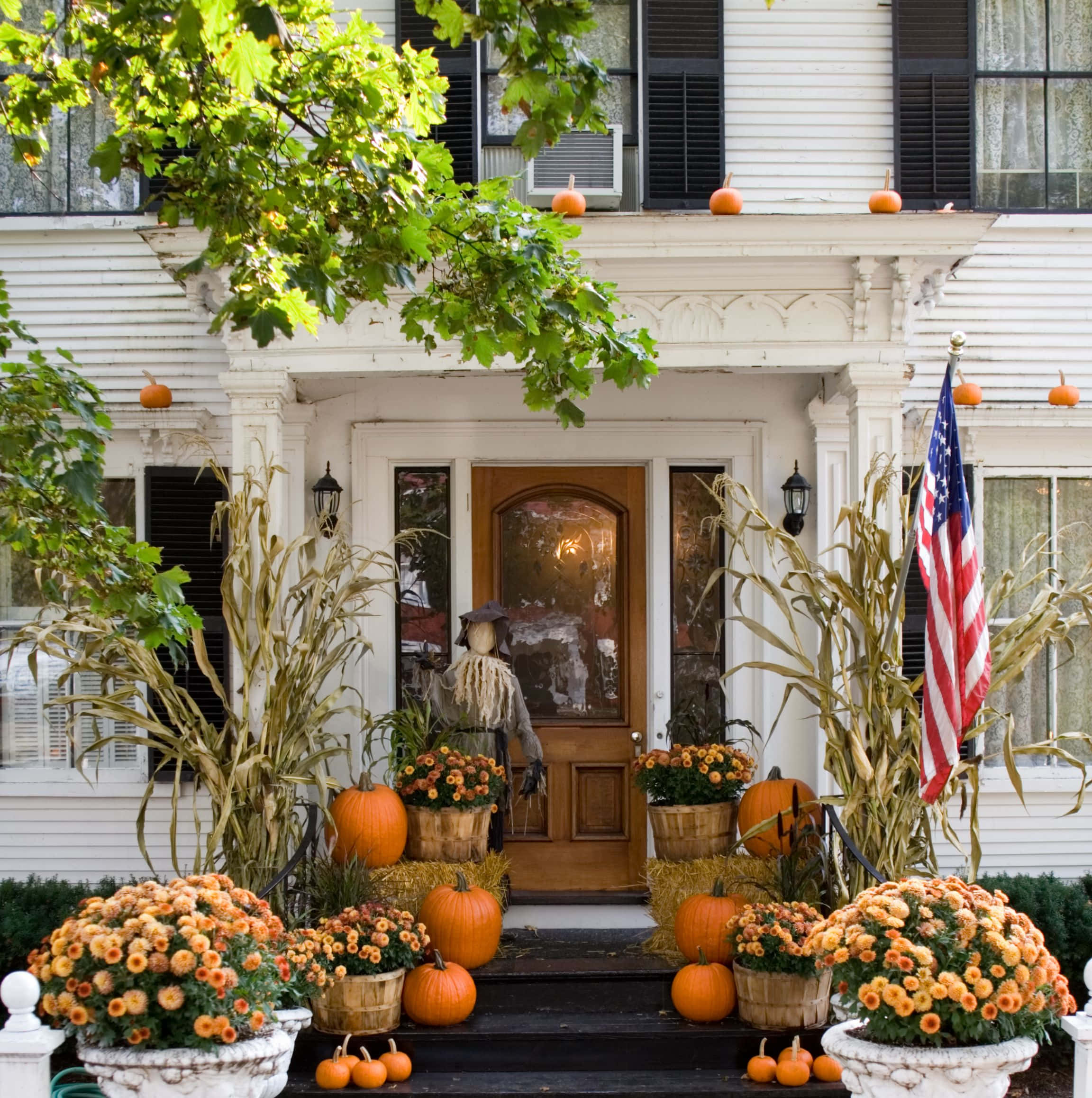 Halloween Yard Decorations 桌布 壁紙 — 迷人的白色房屋門廊裝飾著南瓜、玉米稈和鮮豔的橙色菊花，營造出節日般的秋季歡迎氛圍。