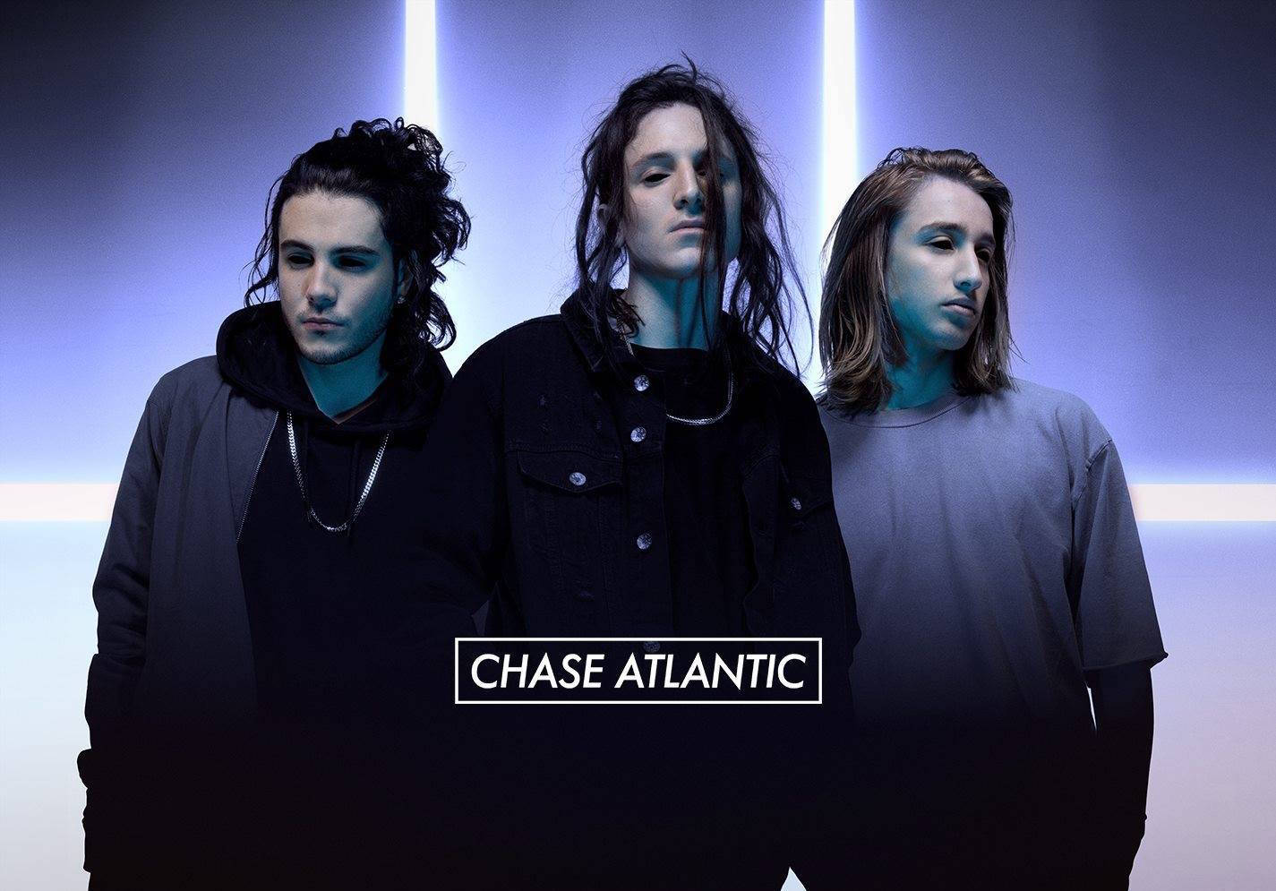 三位身穿深色衣服的音樂家在藍色霓虹燈下，帶有「CHASE ATLANTIC」字樣。