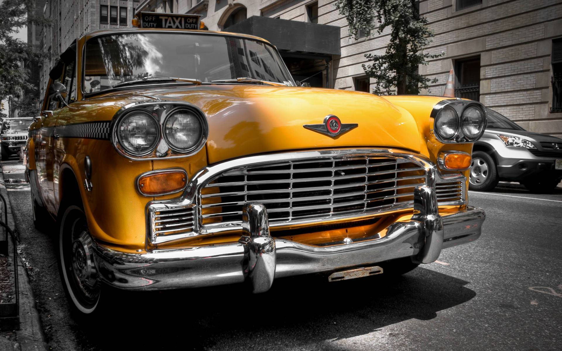 時代遺產：古董 Checker 出租車 壁紙 — 一輛復古黃色計程車，帶有鍍鉻細節，停在陽光明媚的城市街道上。
