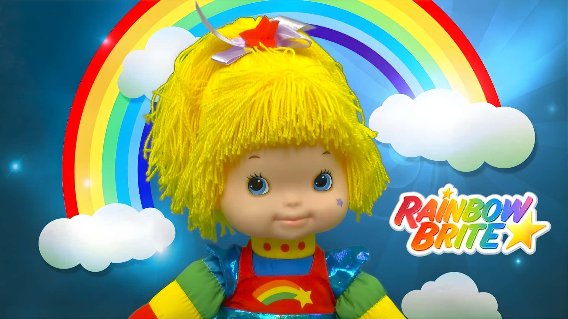  壁紙 — 一個快樂的Rainbow Brite公仔，黃色毛線頭髮和彩虹服裝，站在明亮的彩虹和蓬鬆的雲朵前。