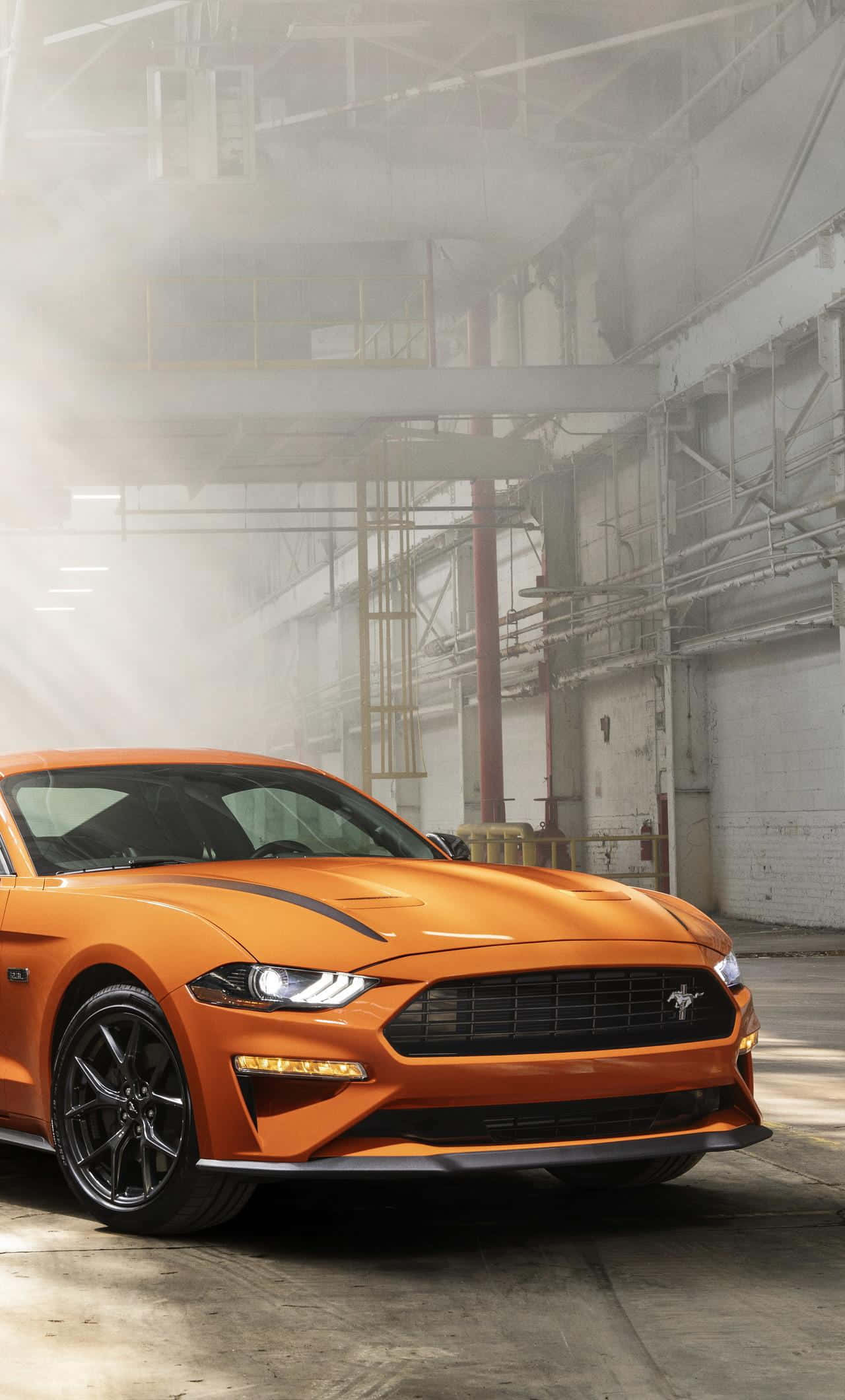 Ford Mustang Ecoboost 桌布 壁紙 — 一輛充滿活力的橙色福特野馬跑車，在霧氣瀰漫的工業倉庫內，於戲劇性的燈光下閃閃發光。