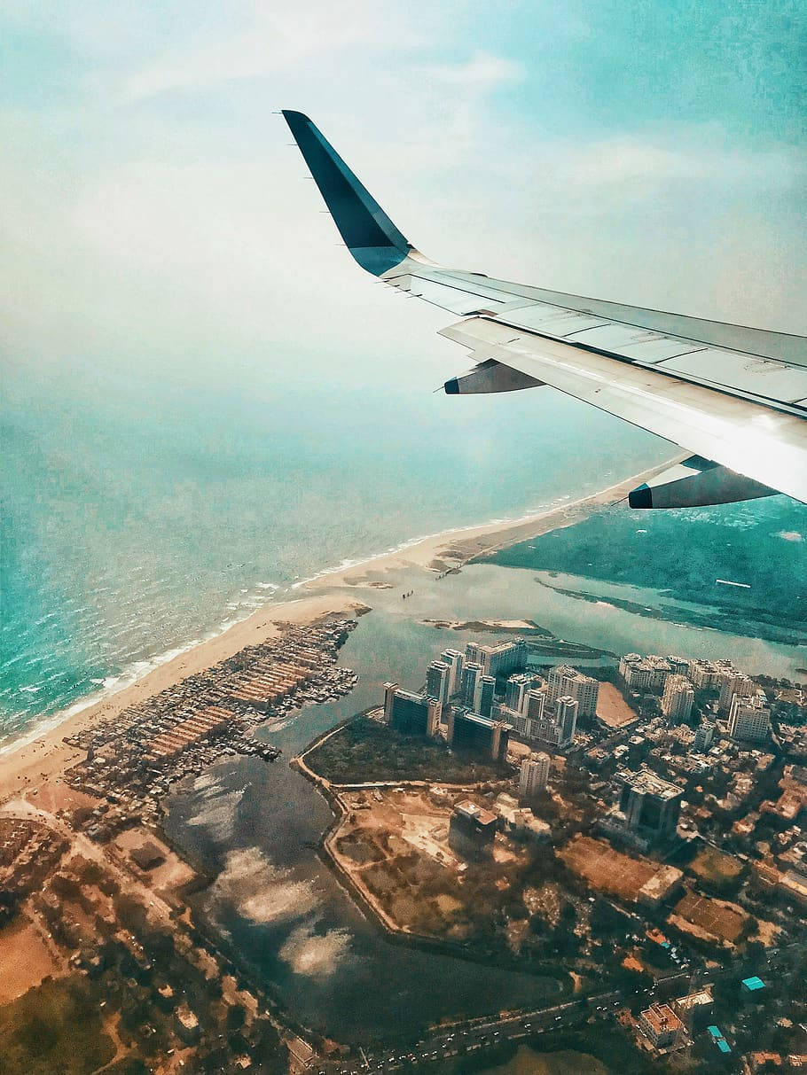 飛機機翼俯瞰沿海城市和藍綠色海洋及沙灘。