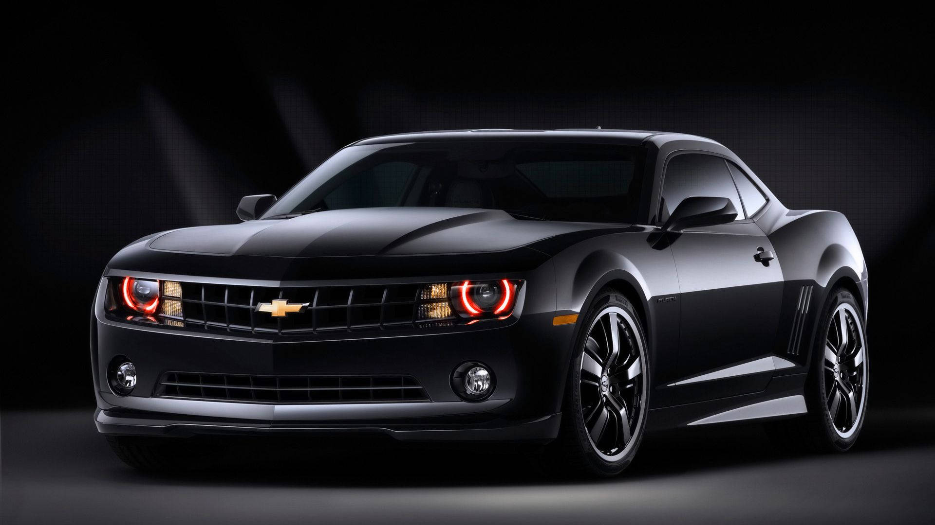 霸氣黑 Chevrolet Camaro 肌肉車 壁紙 — 一架時尚的黑色雪佛蘭 Camaro，帶有發光的紅色頭燈，在黑暗的攝影棚背景下戲劇性地照亮。