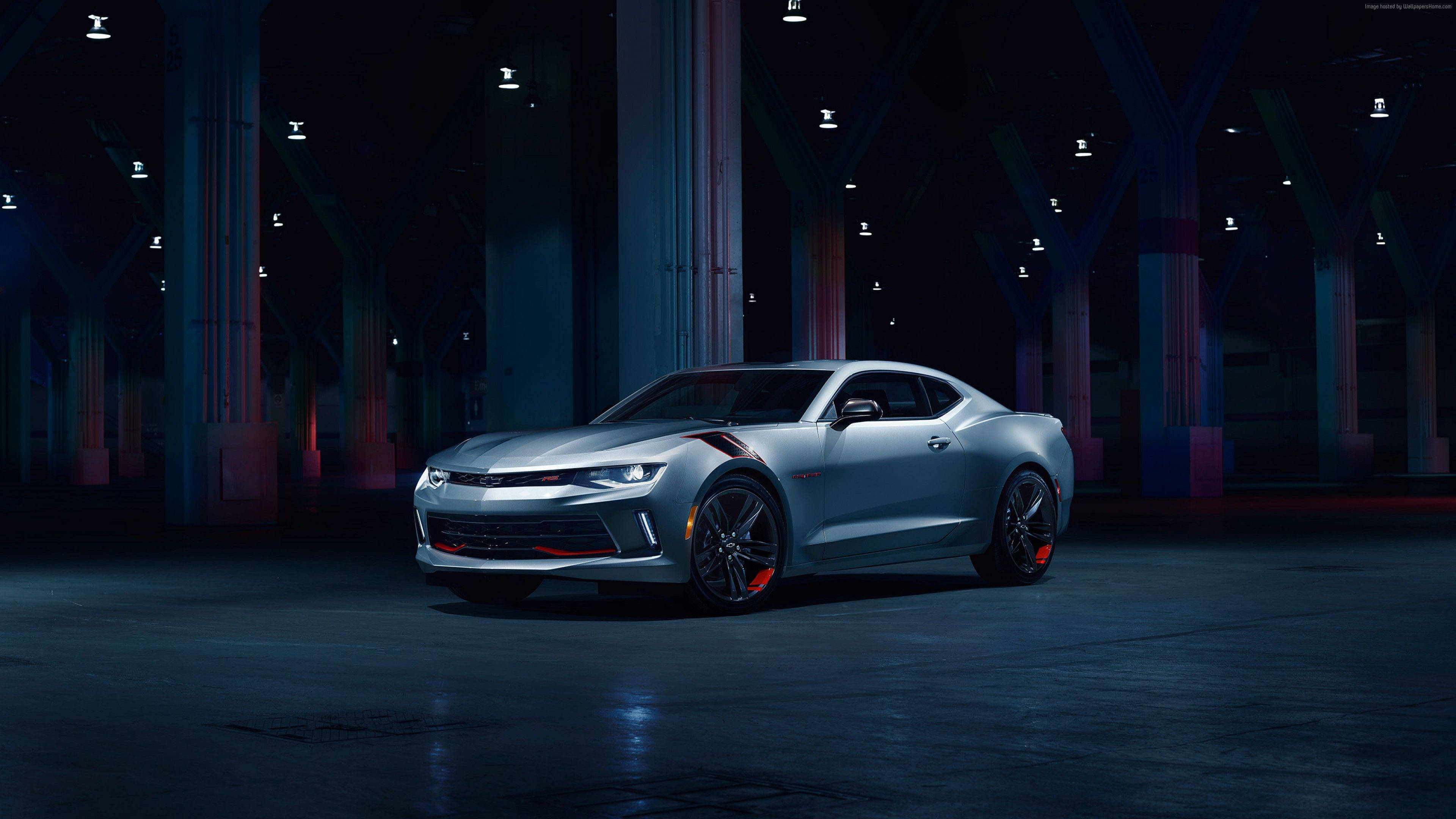 銀色Chevrolet Camaro 4K 壁紙 — 一架流線型的銀色雪佛蘭Camaro跑車在寬敞的工業倉庫中，在戲劇性的藍色和紅色燈光下閃閃發光。