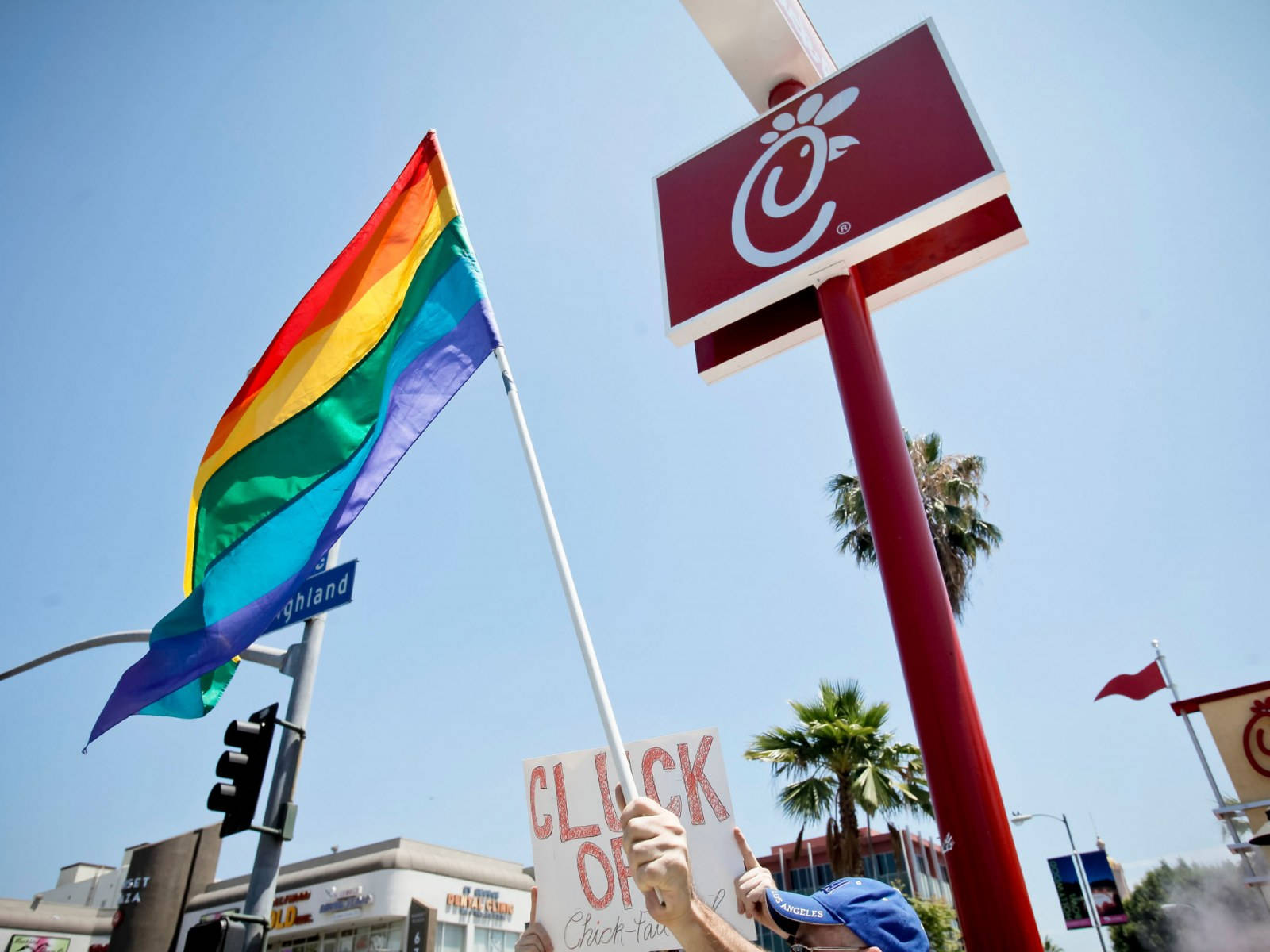 Chick Fil A LGBTQ 旗幟 壁紙 — 一個人在晴朗的藍天下，在Chick-fil-A餐廳前舉著彩虹旗和抗議標語。