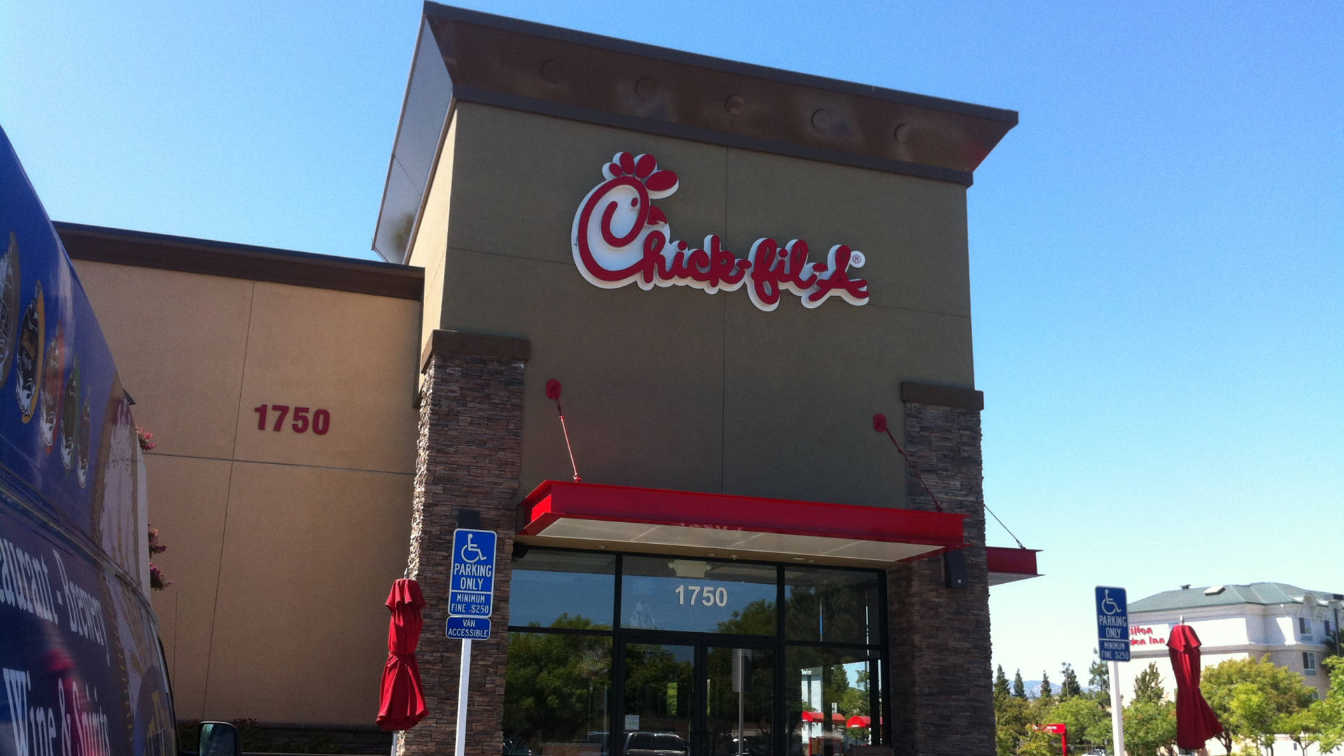 Chick Fil A 快餐 壁紙 — Chick-fil-A 餐廳建築，在晴朗的藍天下，前方有紅色遮陽篷和關閉的雨傘。
