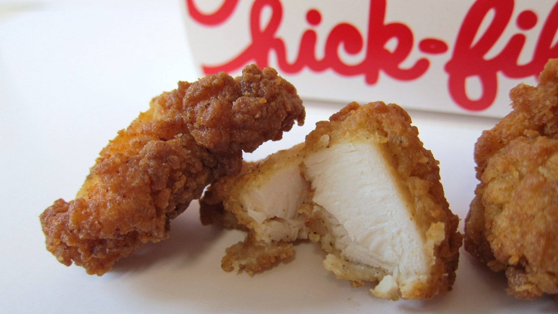 Chick Fil A 新鮮雞塊 壁紙 — 金黃酥脆的炸雞塊，多汁的白肉放在白色碟子上，旁邊有一個Chick-fil-A標誌盒。