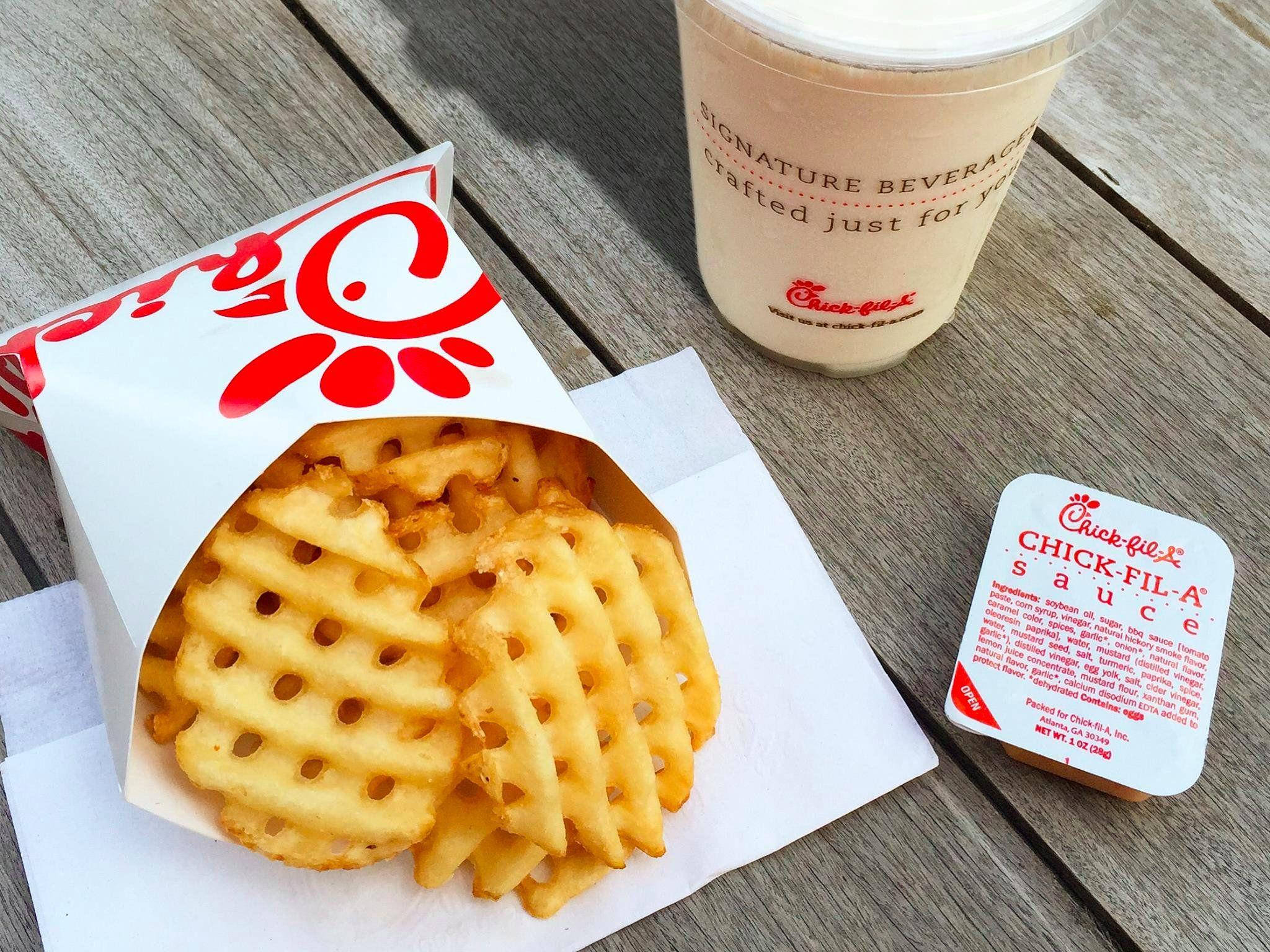 Chick Fil A 橫紋薯條 壁紙 — Chick-fil-A 盒子裡的金黃色窩夫薯條，旁邊放著招牌飲品和醬料包，置於經風化的木桌上。