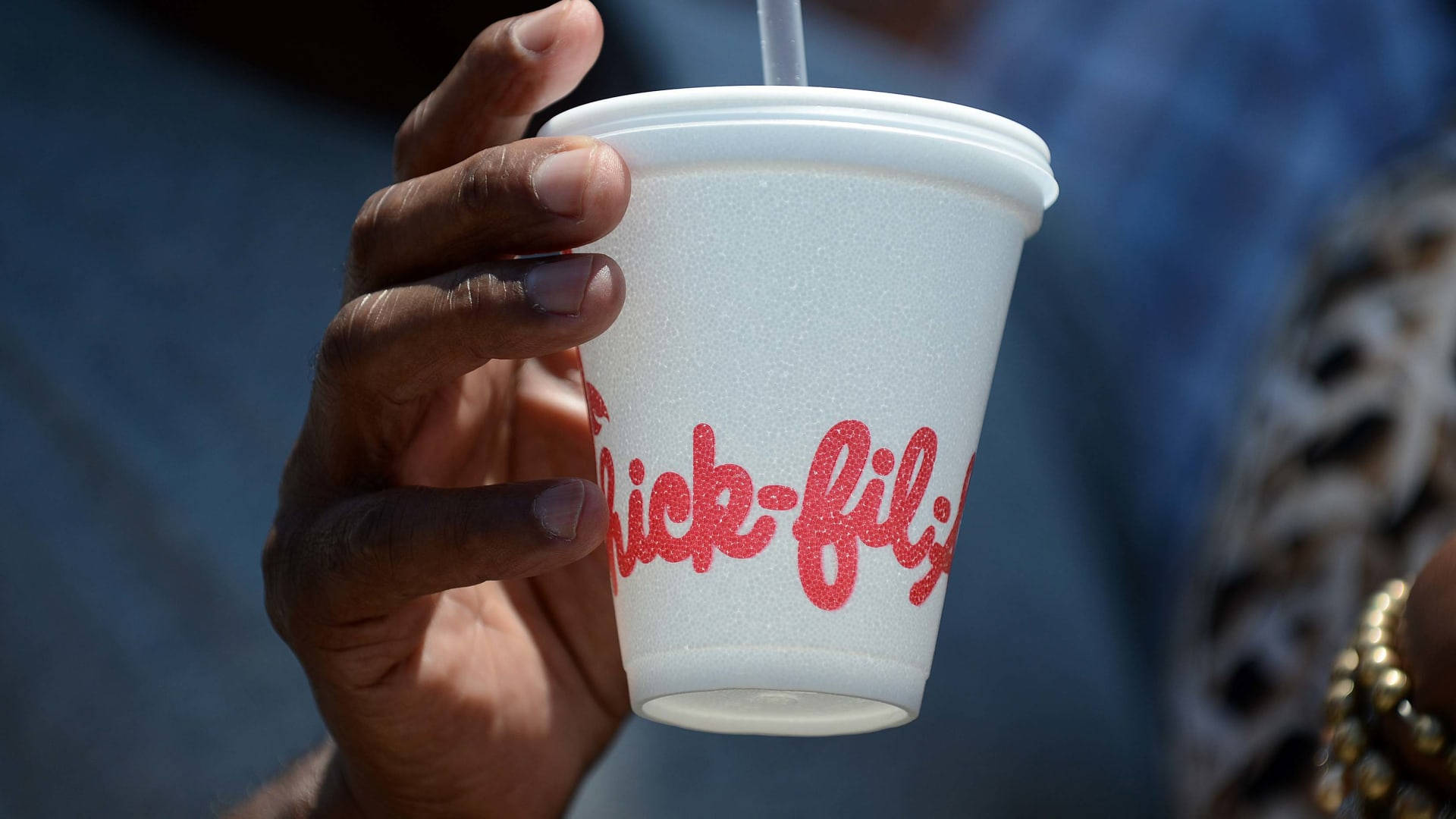 Chick Fil A 泡沫杯 壁紙 — 特寫一隻手拿著帶有吸管的Chick-fil-A泡沫杯，背景模糊。