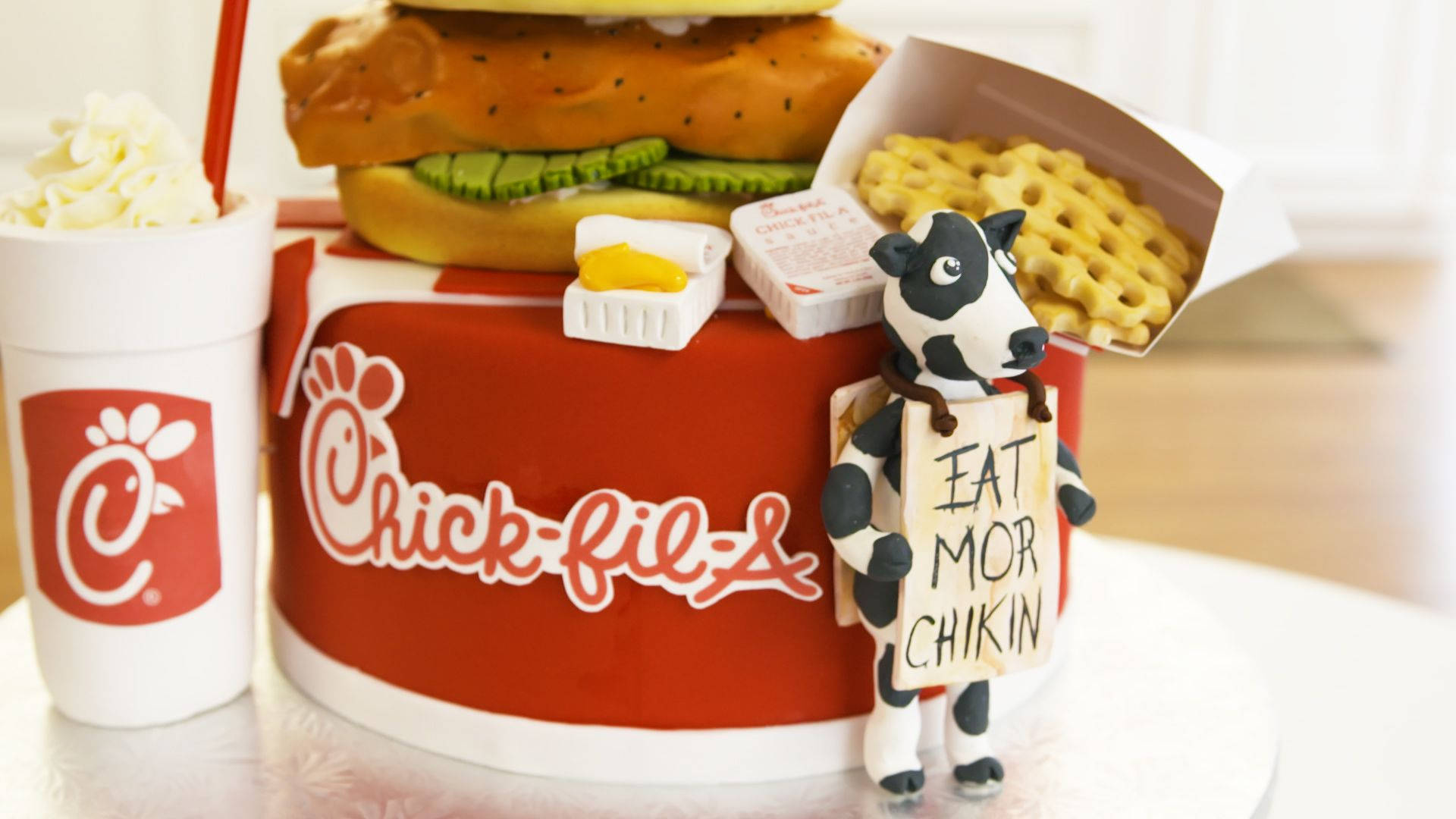 Chick Fil A 覆蓋糖霜蛋糕 壁紙 — 一個奇特的Chick-fil-A主題蛋糕，上面放著一個巨大的漢堡薯條和一隻拿著寫著eat mor chikin牌子的牛。