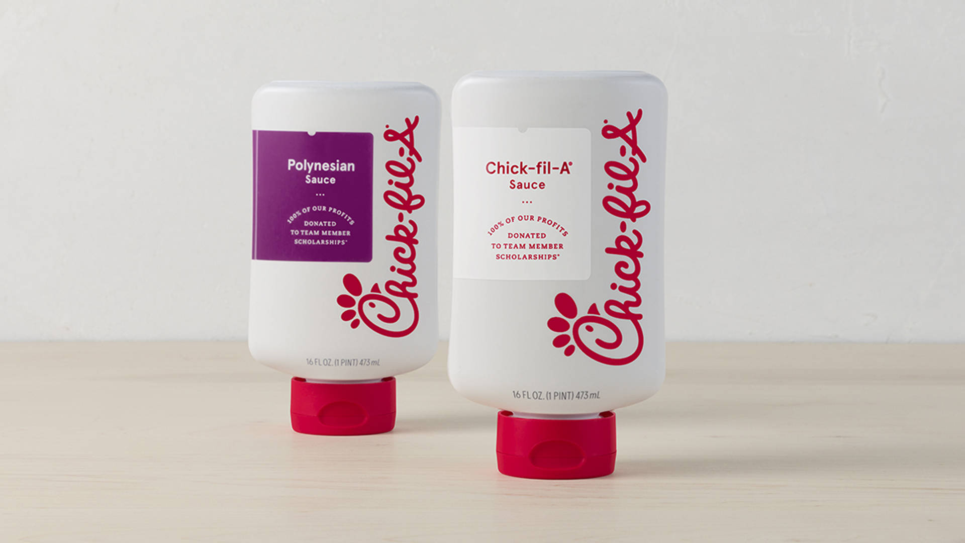 Chick Fil A 醬料 壁紙 — 兩瓶Chick-fil-A醬料瓶，一瓶波利尼西亞風味一瓶原味，並排放在淺色木質表面上，背景是純白牆壁。