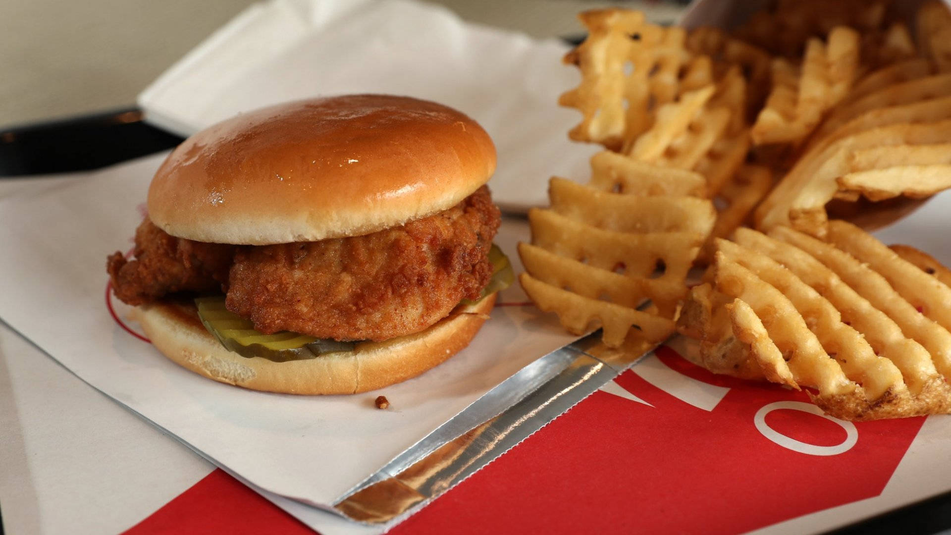 Chick Fil A 魚排三明治 壁紙 — 一個脆皮炸雞三文治配酸瓜，旁邊有窩夫薯條，放在紅白紙托盤上。