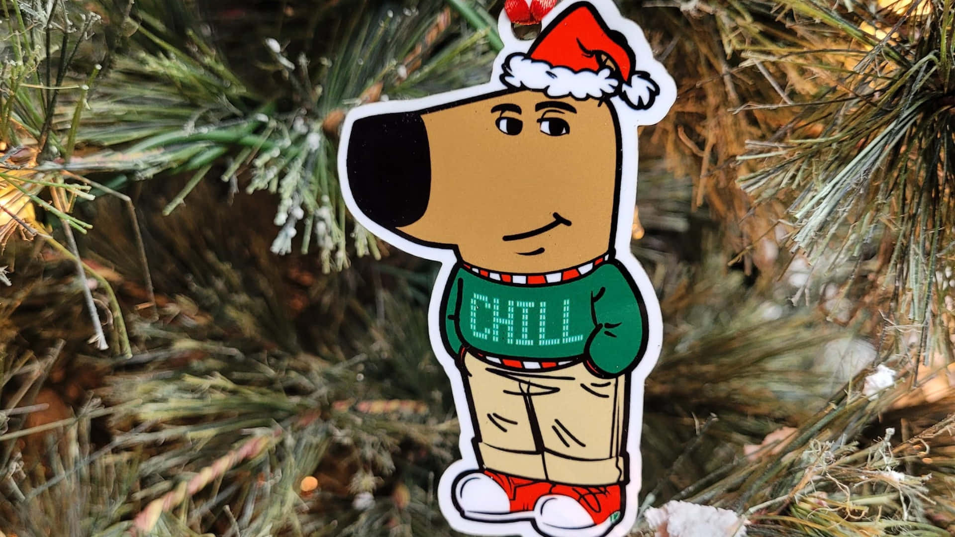 Chill Guy 圣誕裝飾品 壁紙 — 一張卡通狗貼紙，戴著聖誕帽和「CHILL」毛衣，掛在雪松樹枝上。