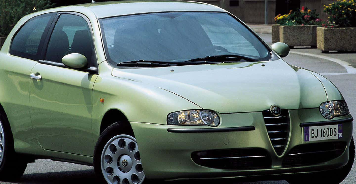 Alfa Romeo 147 桌布 壁紙 — 一架淺綠色嘅Alfa Romeo 147揭背車泊喺鋪砌嘅街道上，背景有花槽。