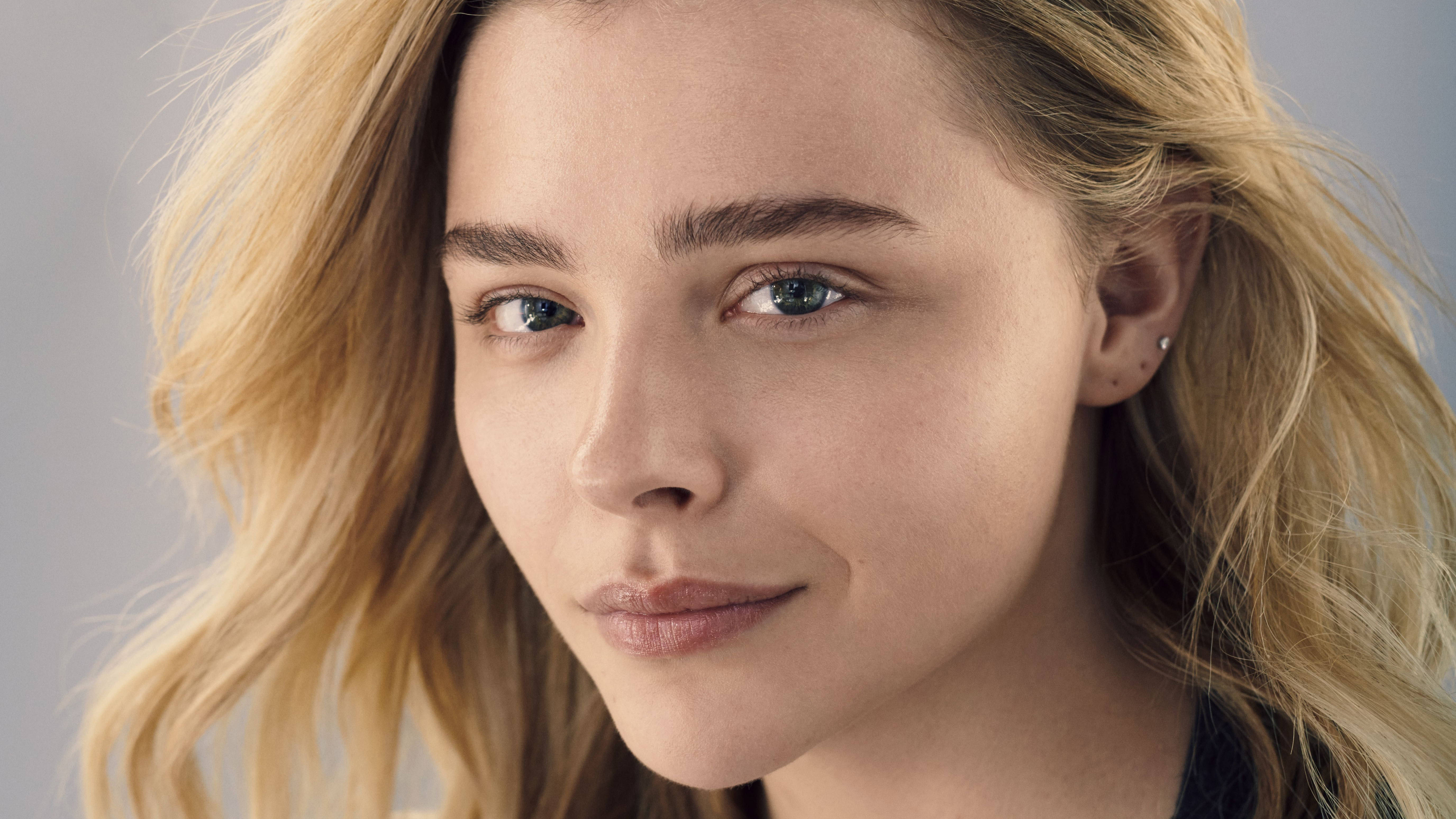 Chloë Grace Moretz 特寫鏡頭 壁紙 — 一位金髮藍眼的年輕女性在灰色中性背景前，柔和地凝視鏡頭的近距離肖像照。