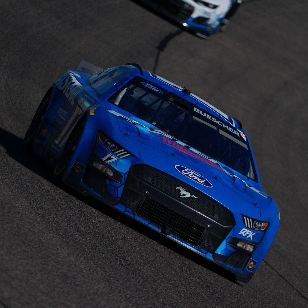 Chris Buescher 斜角視角 壁紙 — 一架充滿活力的藍色福特野馬賽車在賽道上疾馳，背景中可見另一輛車。