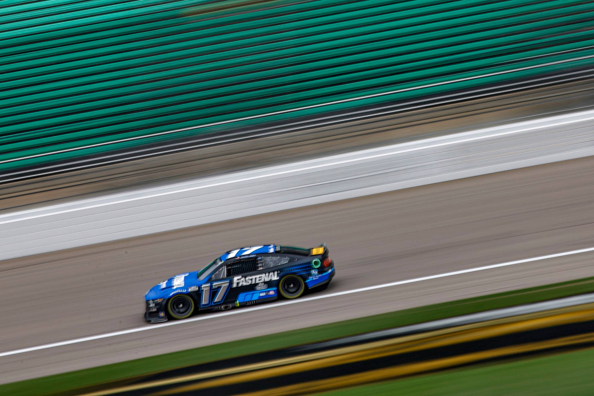 Chris Buescher 高速疾馳 壁紙 — 一輛藍色賽車，號碼17，在賽道上飛馳，賽道有模糊的綠色護欄和白色線條。