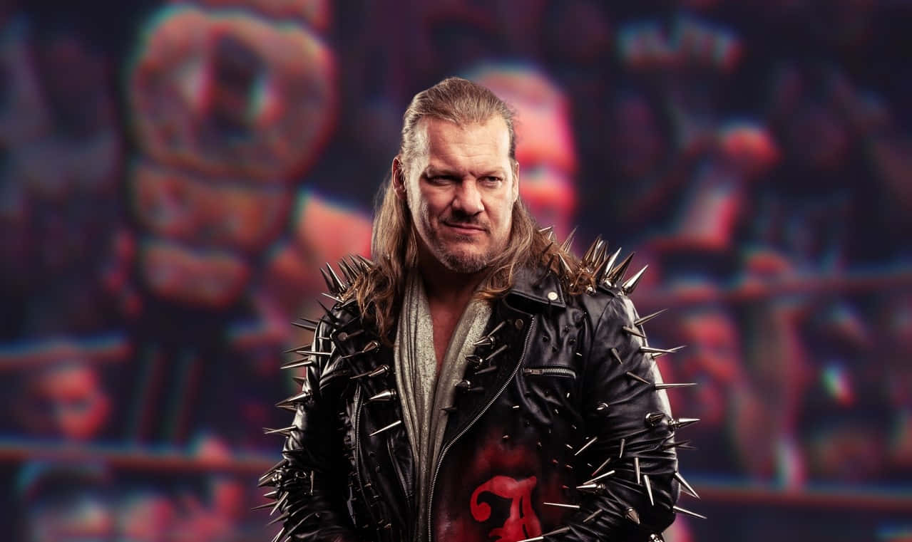 Chris Jericho AEW 鬃髮尖夾克壁紙 壁紙 — 一個長髮的兇猛摔角手，穿著帶有尖刺的皮褸，背景是模糊的摔角場館。