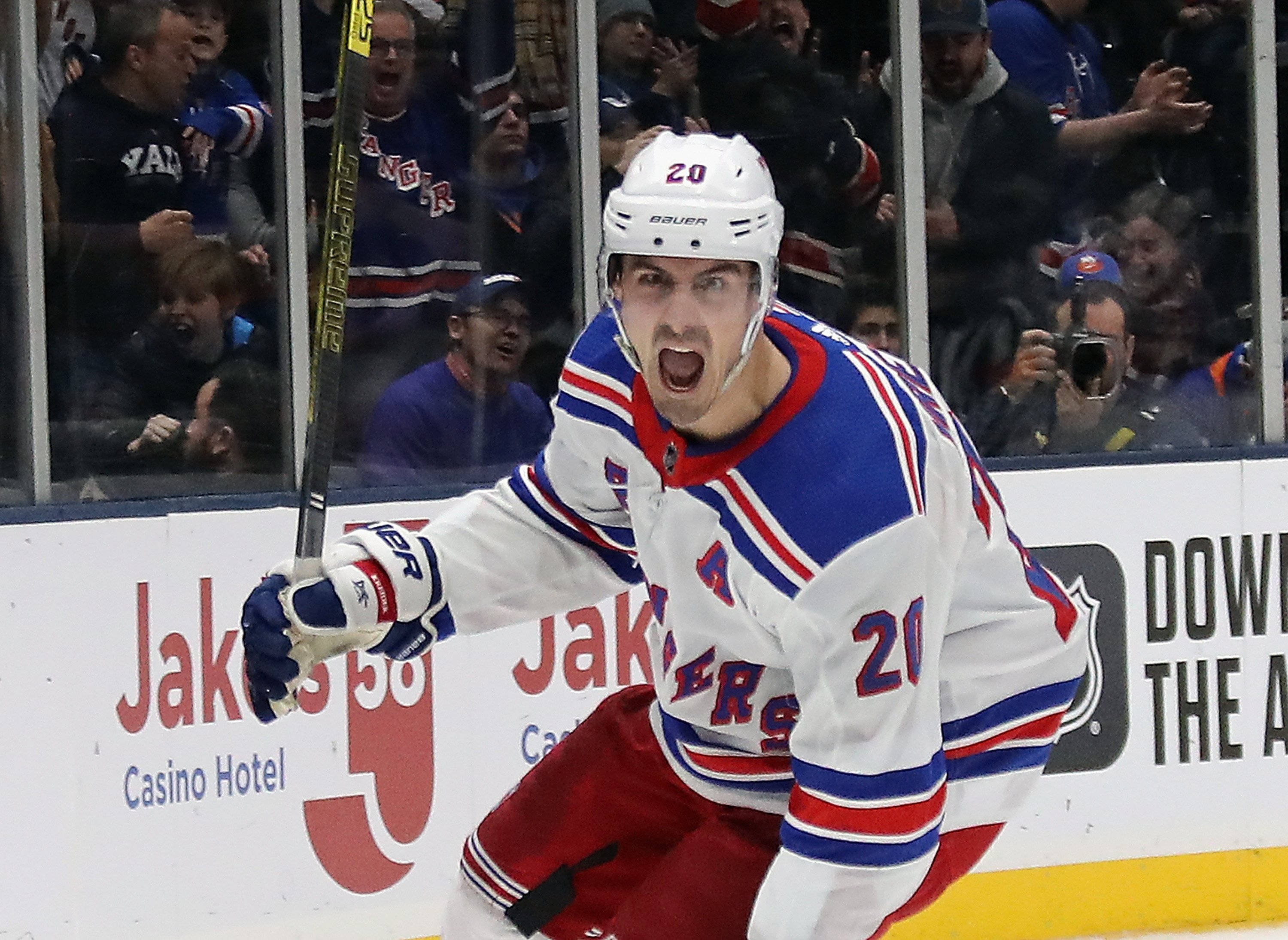 Chris Kreider 紐約遊騎兵隊冰球賽事 壁紙 — 一名穿著流浪者隊球衣的冰球運動員在冰上勝利咆哮，球迷在玻璃後面歡呼。