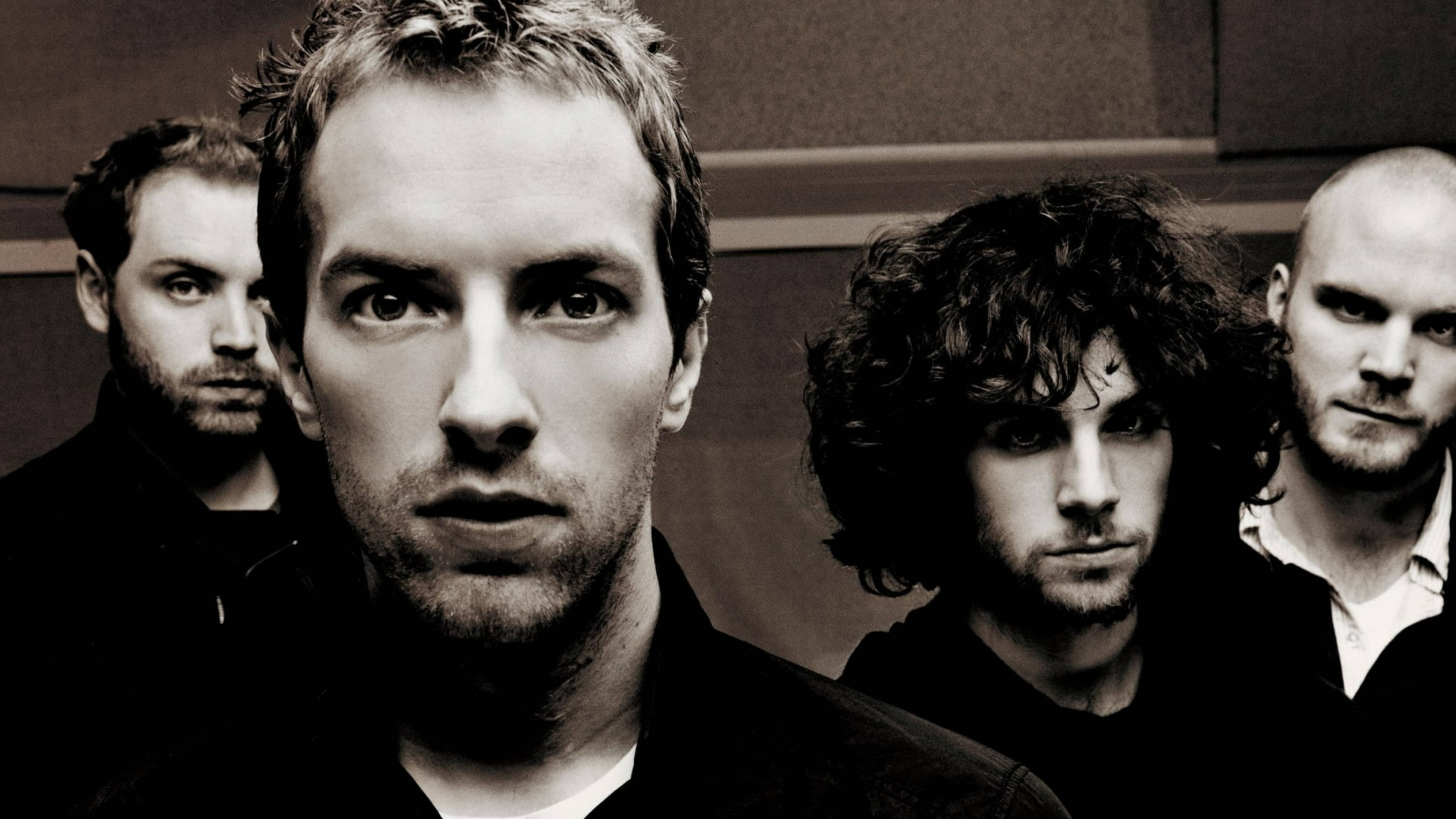 Chris Martin 与 Coldplay 樂隊 壁紙 — 四個男人在黑白鮮明的肖像照中，以強烈的眼神凝視著樸素的牆壁。