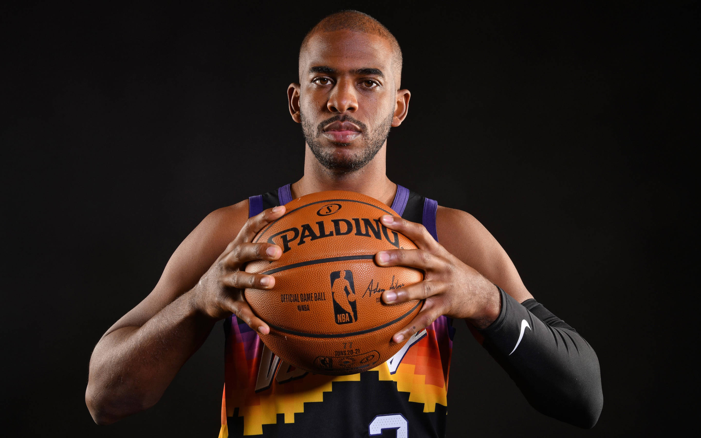 Chris Paul 鳳凰隊黑色球衣 壁紙 — 一名身穿太陽隊球衣的籃球運動員，在黑色背景下專注地拿著一個Spalding籃球。