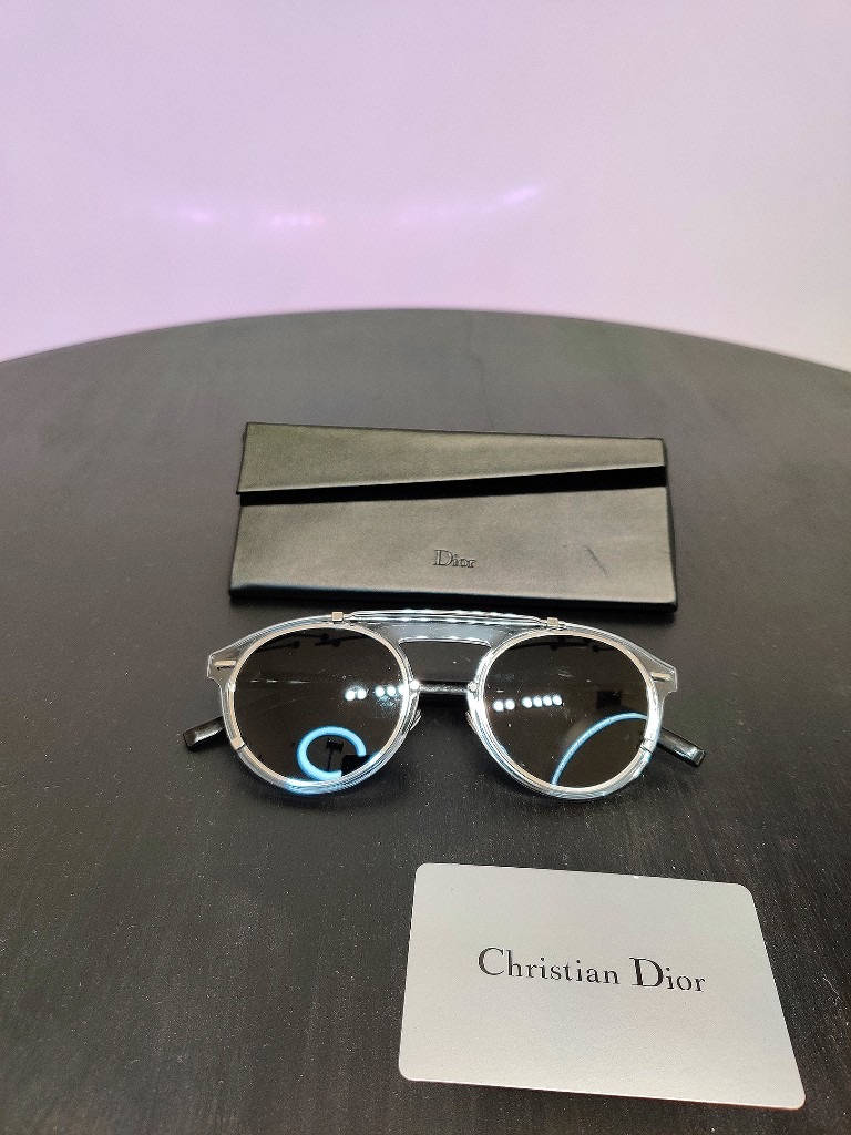 Christian Dior 圓形太陽眼鏡 壁紙 — 優雅的Christian Dior太陽眼鏡，配以銀色鏡框和深色鏡片，放置在深色木質表面上，旁邊是其品牌眼鏡盒和卡片。