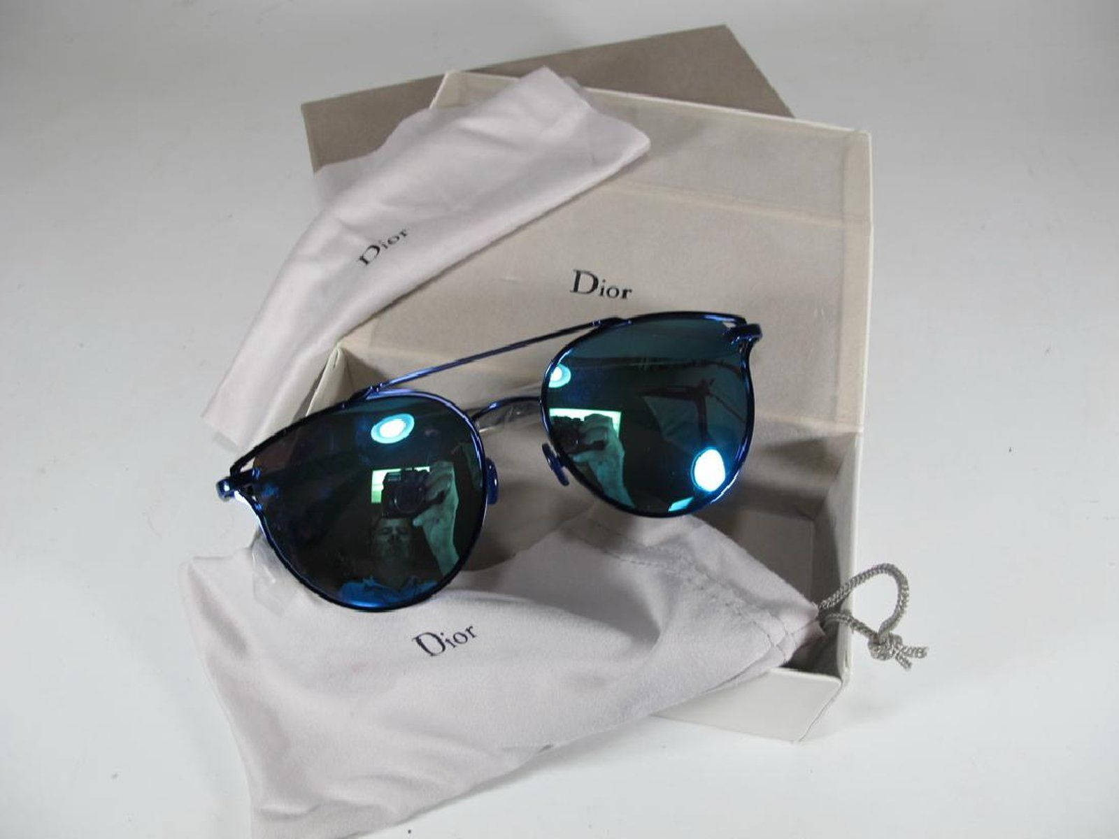 正規 Christian Dior 黑色太陽眼鏡 壁紙 — 藍色鏡面Dior太陽眼鏡優雅地放在品牌布料上，旁邊是打開的包裝，背景為潔白乾淨。