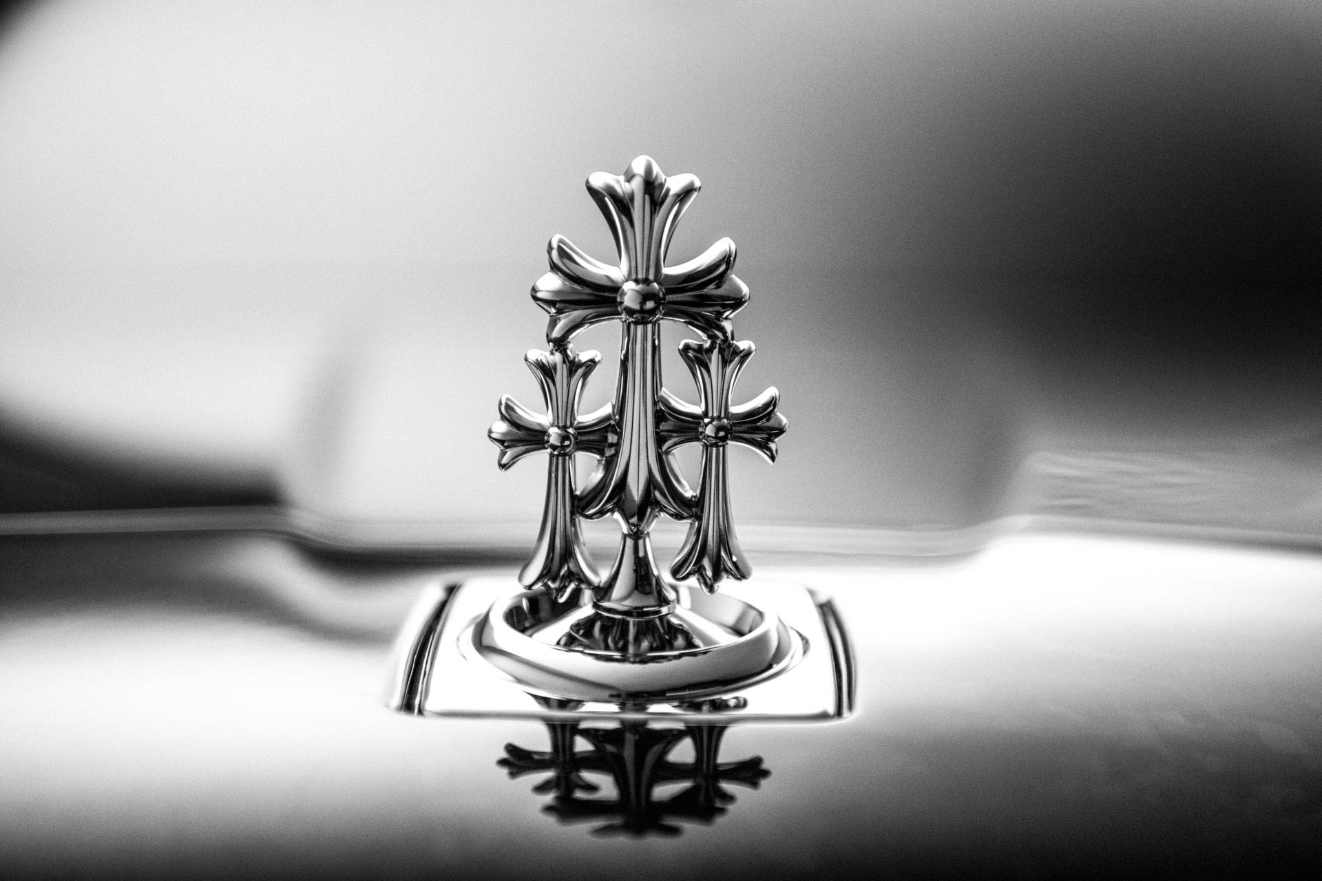 Chrome Hearts 展示人偶 壁紙 — 一個鍍鉻勞斯萊斯格柵飾件的單色特寫，上面有三個華麗的十字架，反射在拋光表面上。