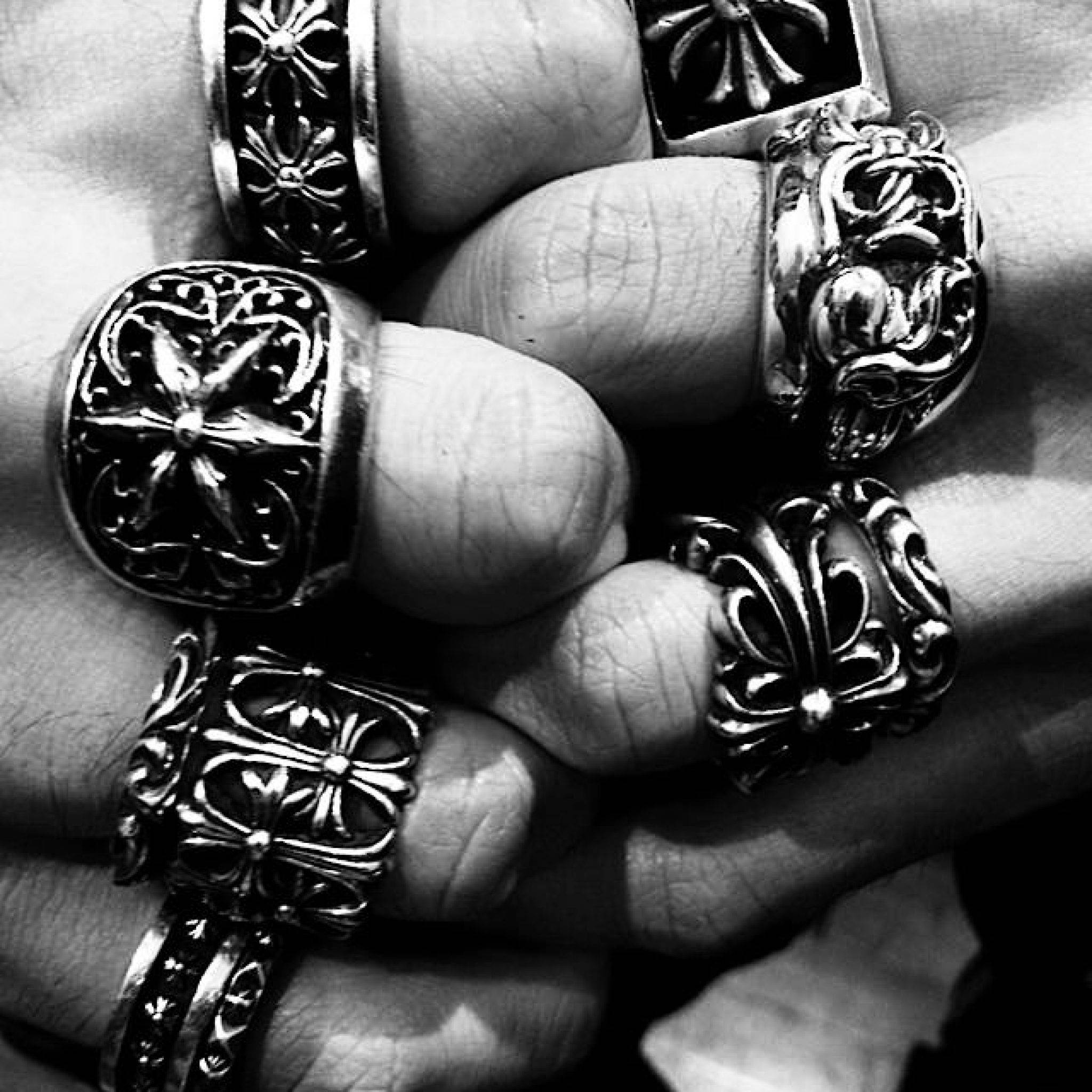 Chrome Hearts 戒指 壁紙 — 一隻手嘅黑白特寫鏡頭，手上戴住華麗、精緻嘅戒指，上面有複雜嘅花卉同幾何圖案。