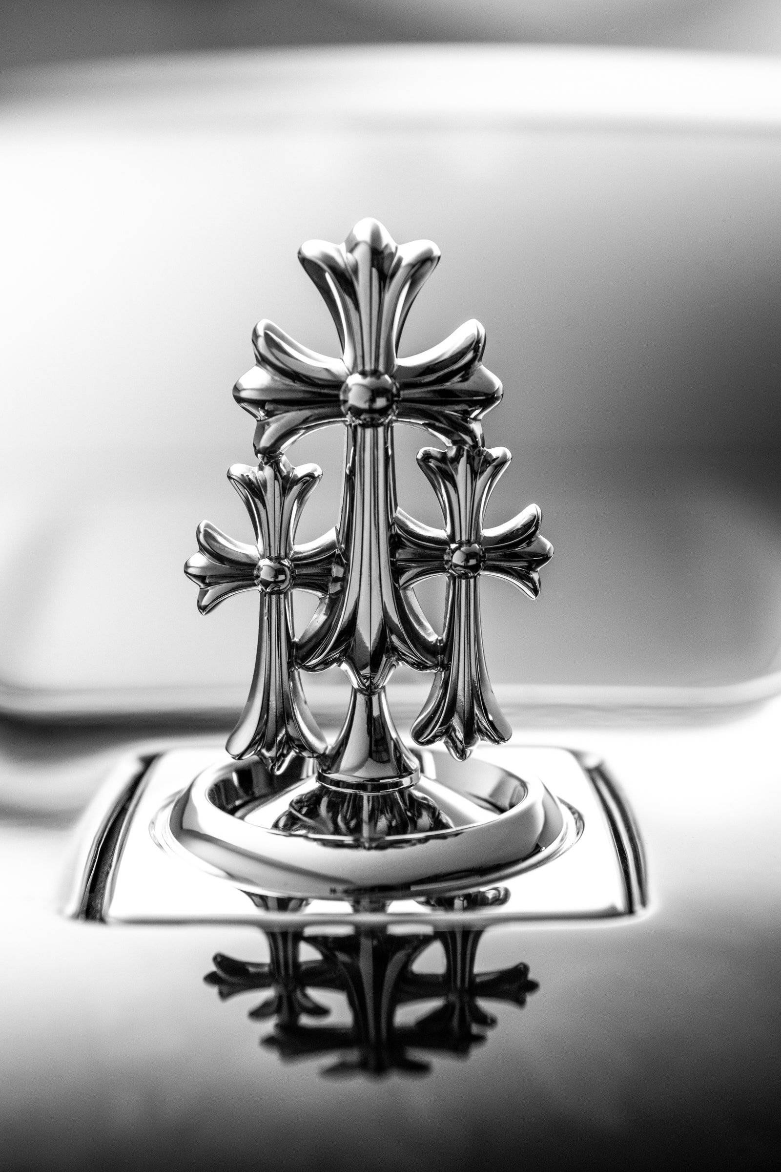 Chrome Hearts 設計於 Rolls Royce 車內 壁紙 — 汽車引擎蓋上鍍鉻十字標誌的單色特寫，具有銳利反射和淺景深。