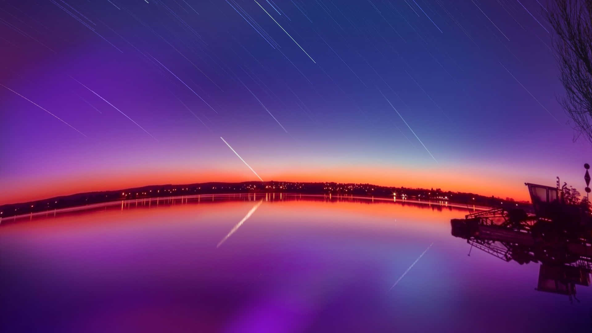 暮色中湖面上的星軌，城市燈光倒映在水中。