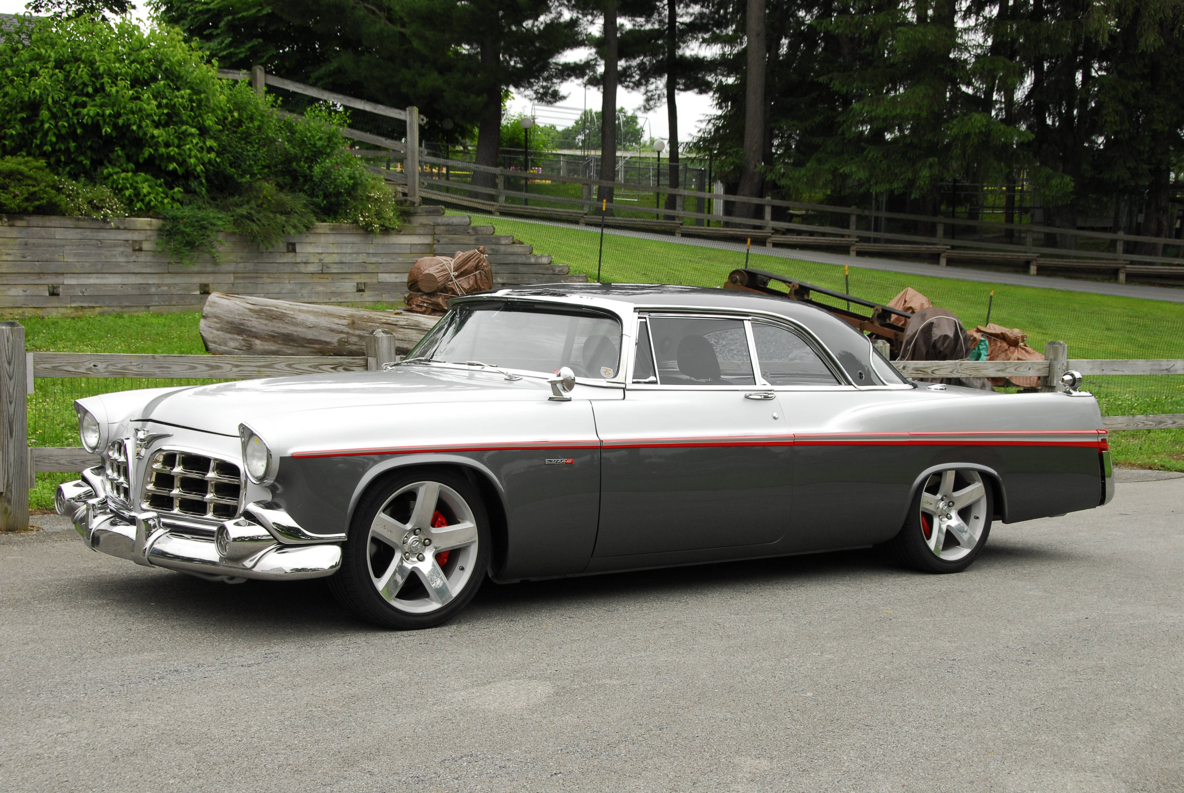 復古 Chrysler 300 壁紙 — 一輛時尚的銀灰色經典汽車，帶有紅色飾邊和定制輪圈，停在木柵欄和綠植旁的碎石車道上。