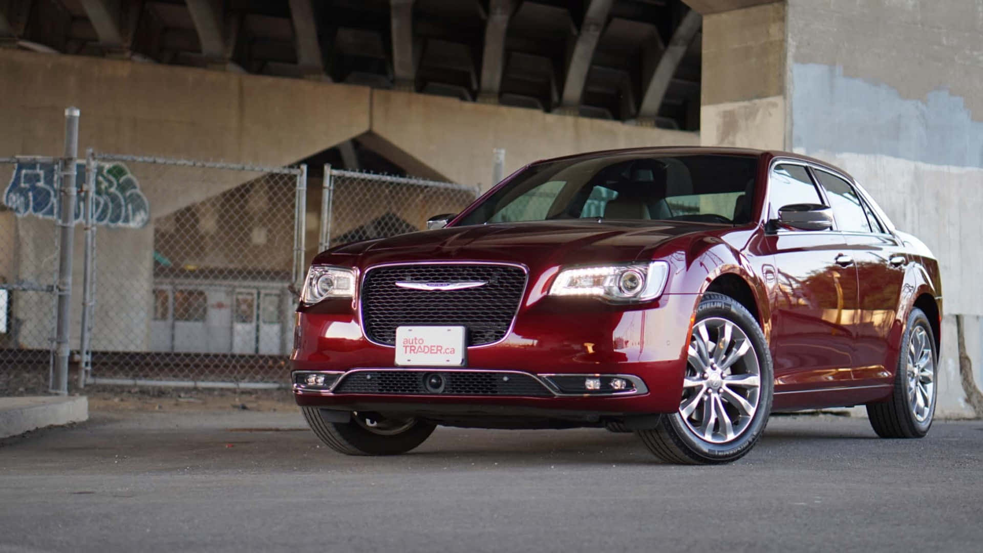 Chrysler 300C 豪華轎車 壁紙 — 一架亮紅色嘅Chrysler房車泊咗喺混凝土天橋下面，後面嘅鐵絲網圍欄上有塗鴉。