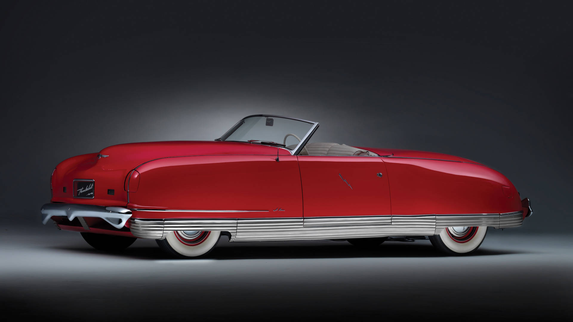 Chrysler Thunderbolt 車款 壁紙 — 一輛光澤的紅色復古敞篷車，帶有鍍鉻飾條和白邊輪胎，在暗色漸變背景下的攝影棚燈光中閃耀。