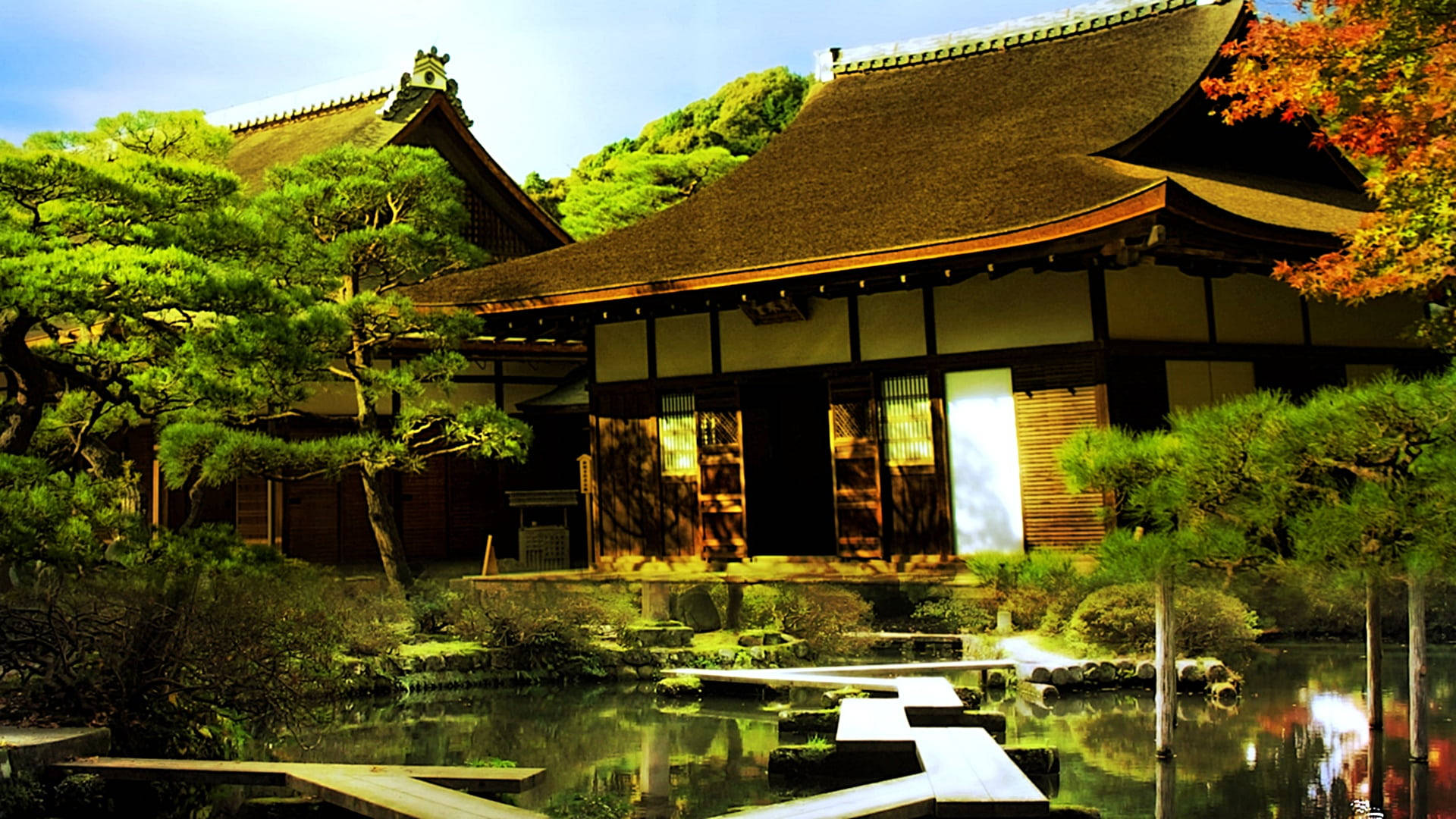 中式宅院與池塘 壁紙 — 傳統日本寺廟，擁有彎曲屋頂和木樑，周圍環繞著秋樹和反射池塘。