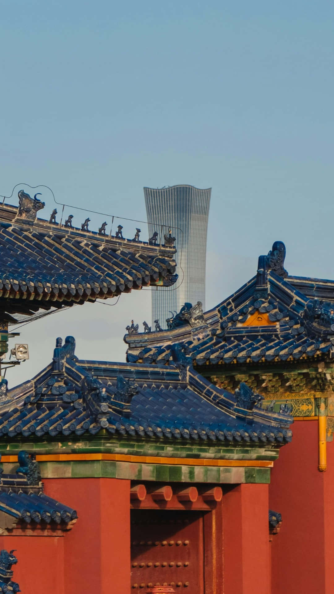  壁紙 — 傳統中式寺廟屋頂，藍色瓦片和紅色牆壁，在晴朗的藍天下與現代玻璃摩天大樓形成對比。