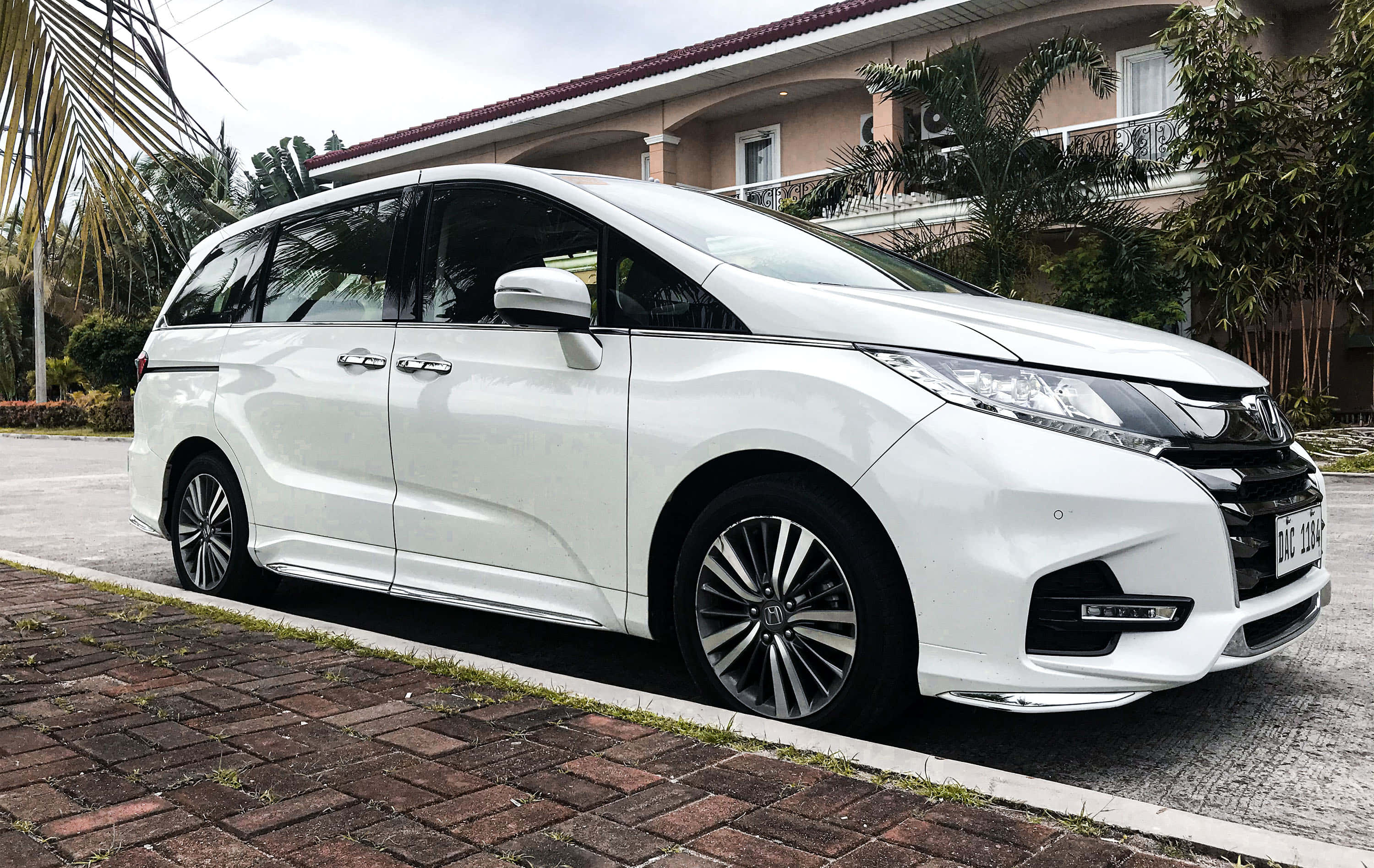 Honda Odyssey 桌布 壁紙 — 一架純白色本田Odyssey小型貨車停泊在磚砌車道上，旁邊是帶有棕櫚樹的熱帶房屋。