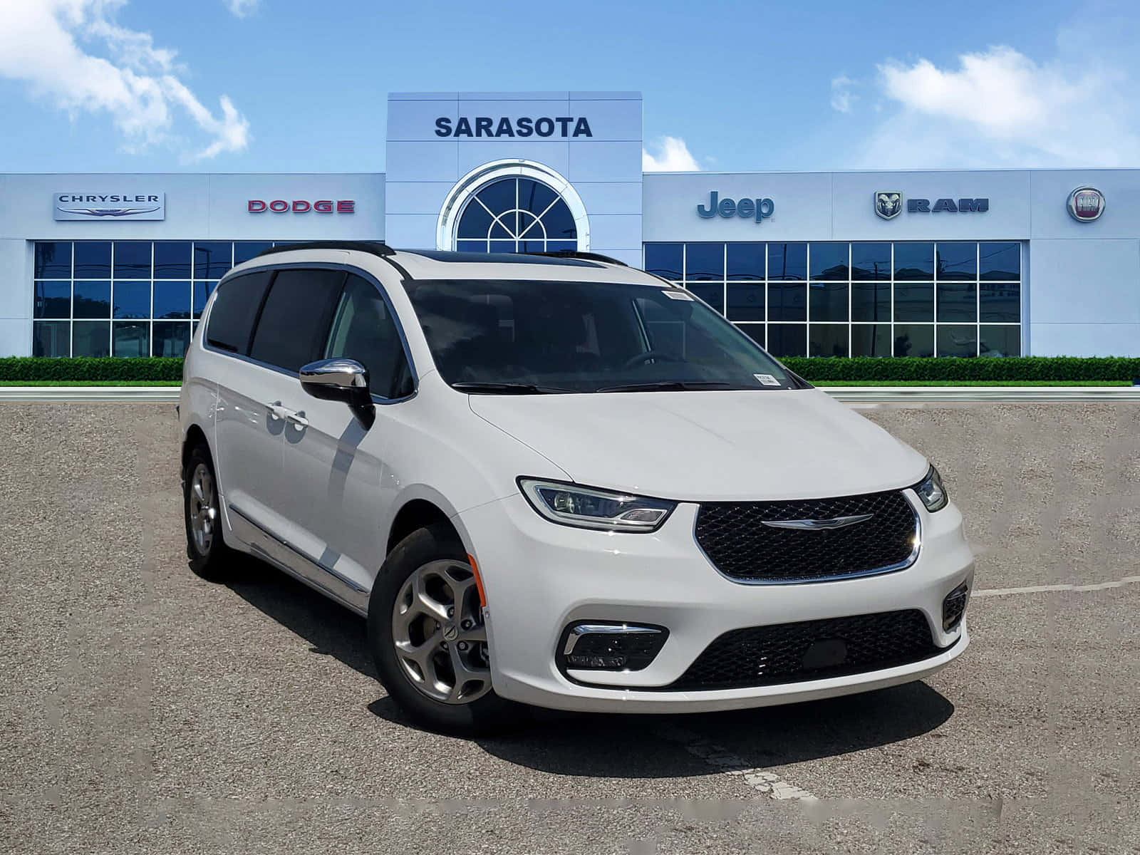 Chrysler Pacifica 桌布 壁紙 — 一輛純白色的 Chrysler Pacifica 小型貨車在明亮陽光下閃閃發光，停泊在現代化經銷商前，上方是清澈的藍天。