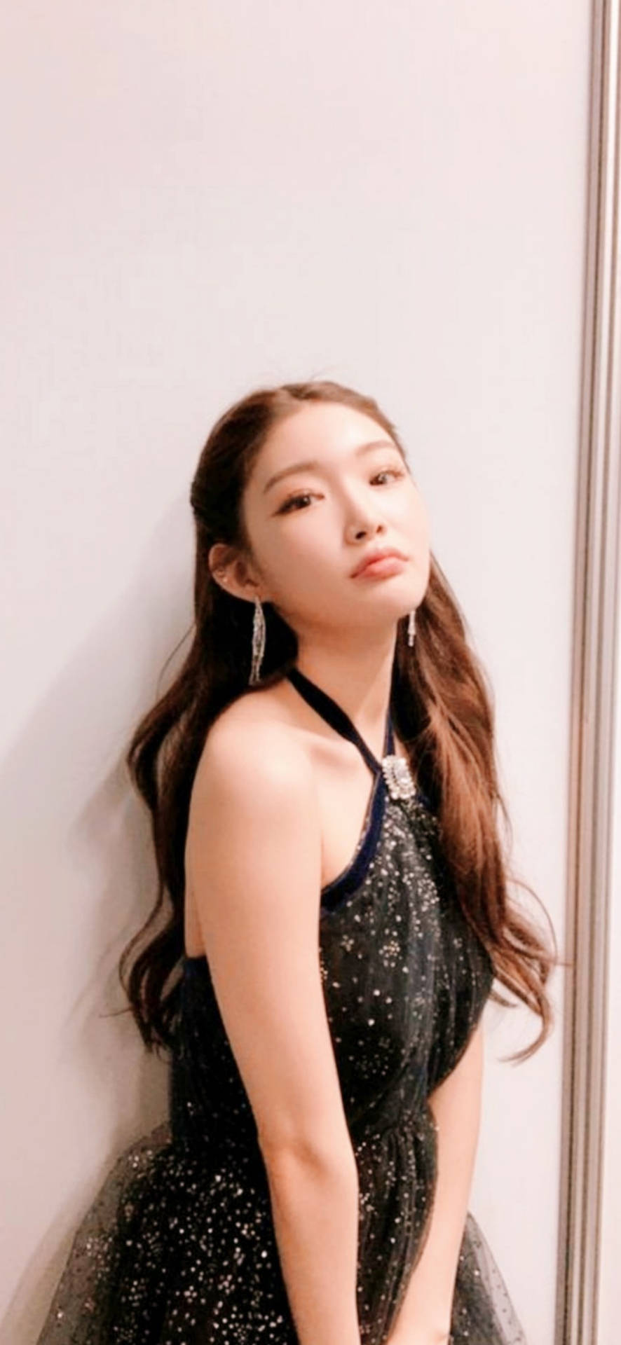 身穿閃亮黑色連衣裙的年輕女士靠著牆。