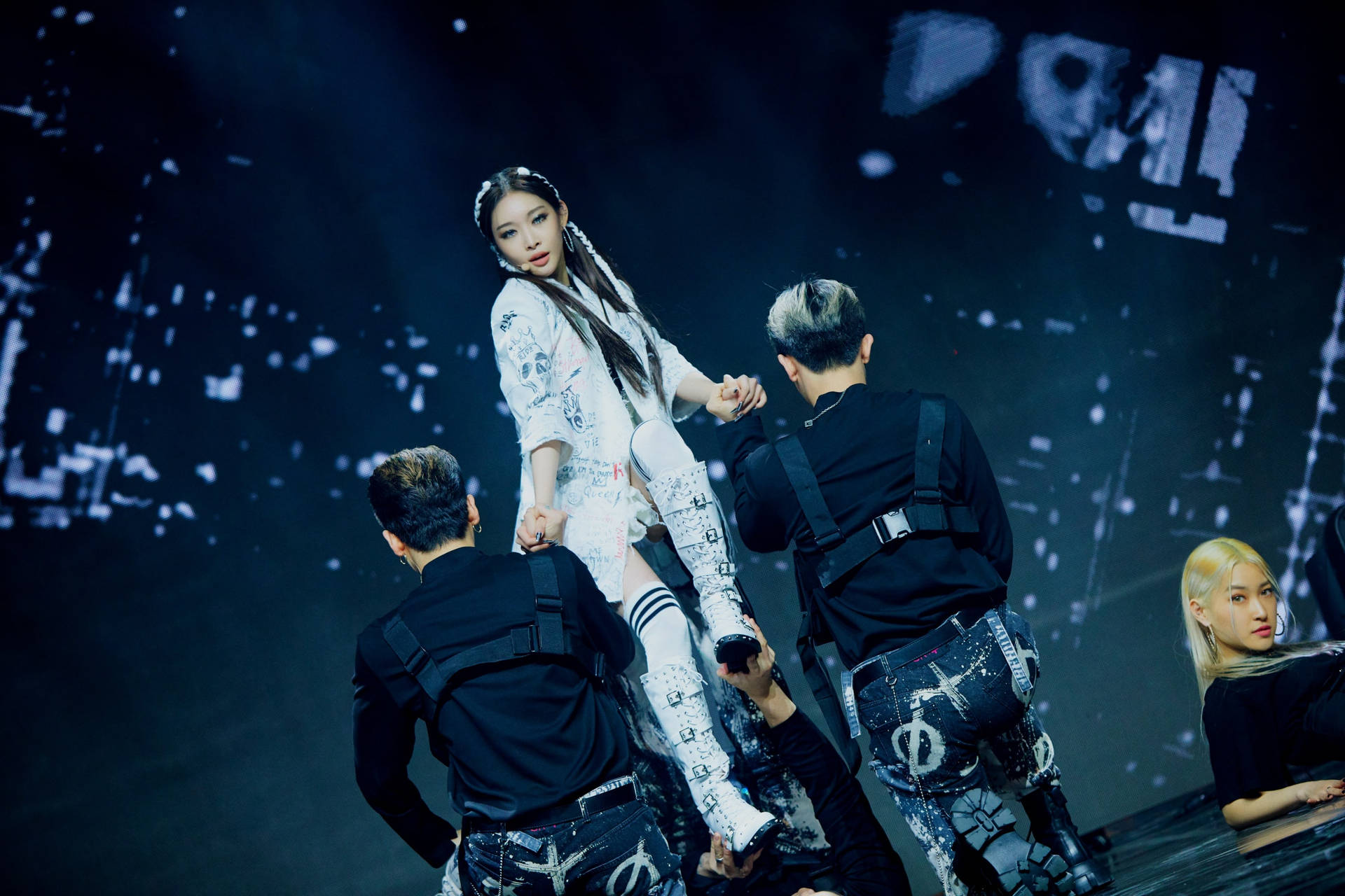 K-pop 舞者在黑暗舞台上，在發光背景前表演編排好的托舉動作。