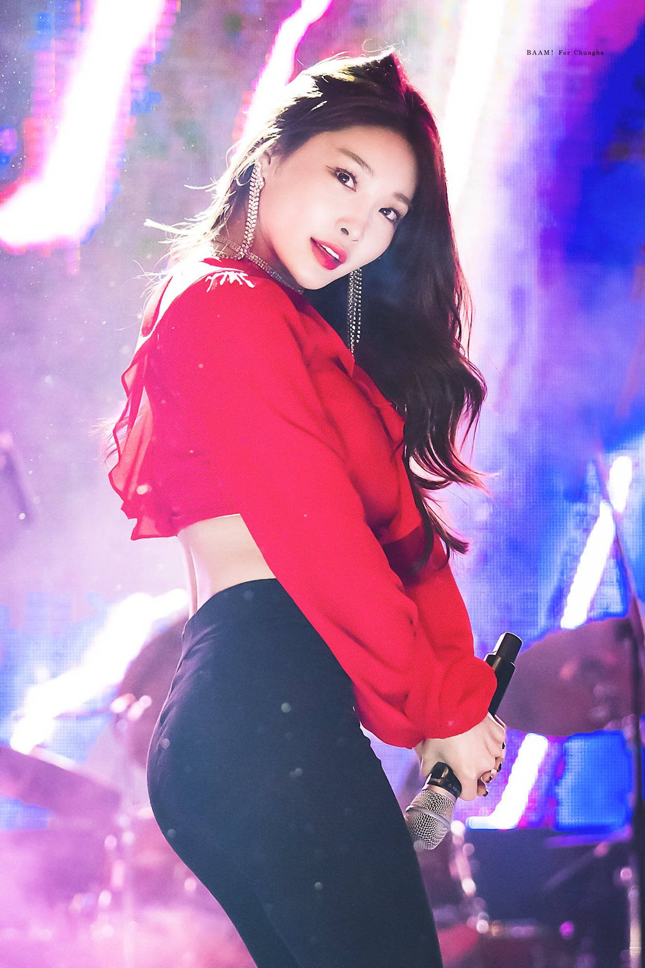 K-pop表演者身穿紅色上衣和黑色褲子在彩色燈光下於舞台上拿著麥克風。