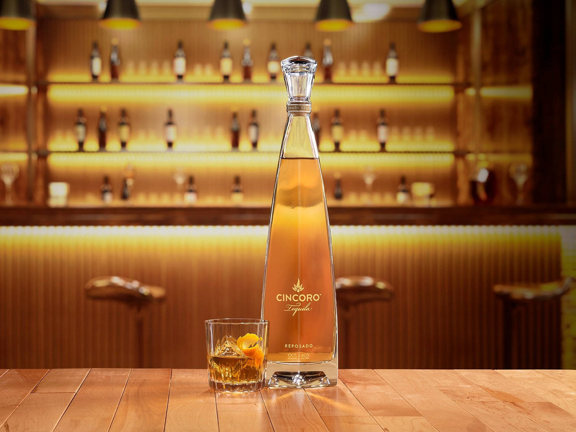 Cincoro Reposado龍舌蘭酒瓶和帶有冰塊和橙裝飾的玻璃杯在木製吧檯上。