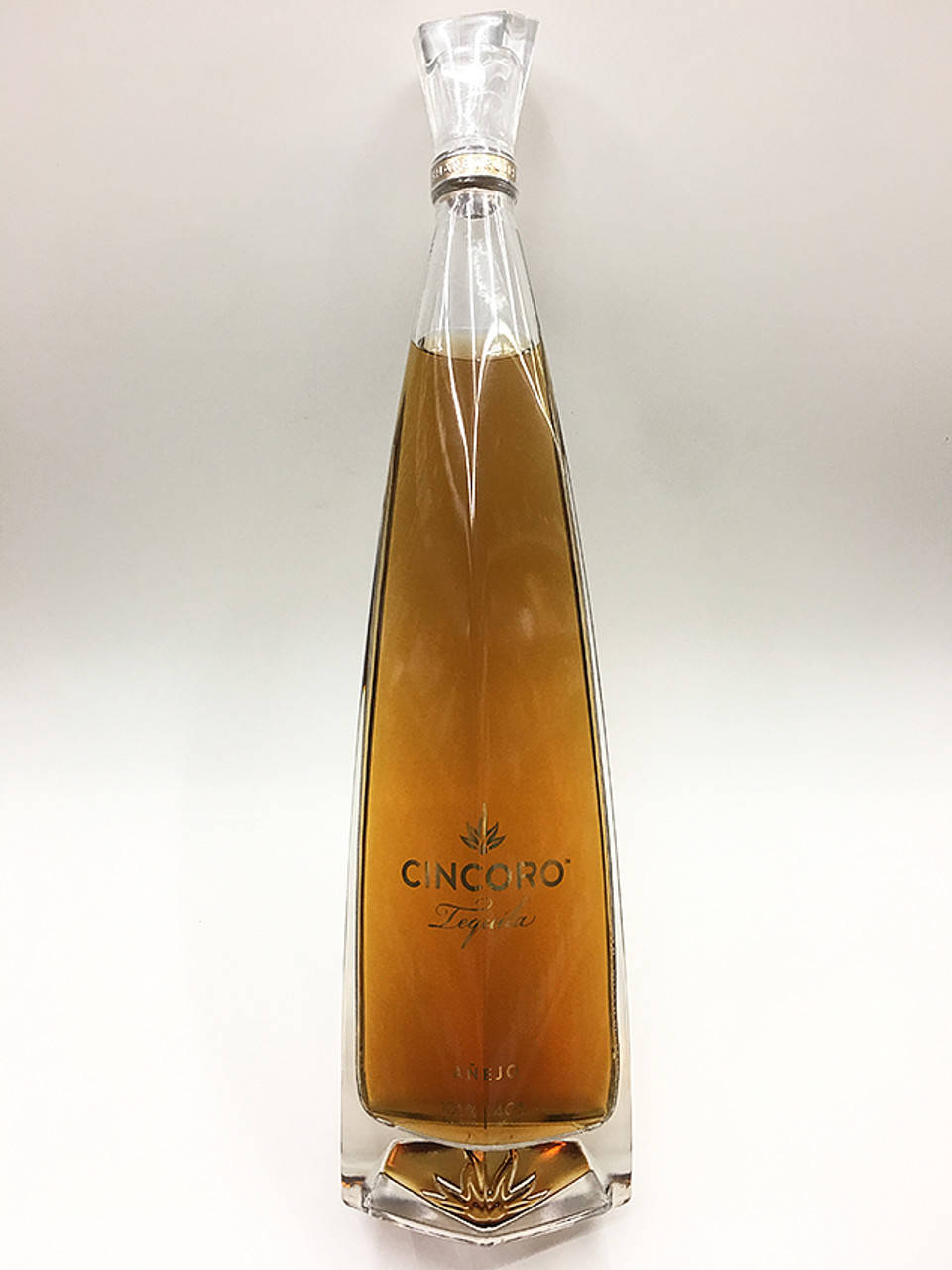 一個透明玻璃瓶Cincoro Tequila，裝有金色液體，背景為白色。