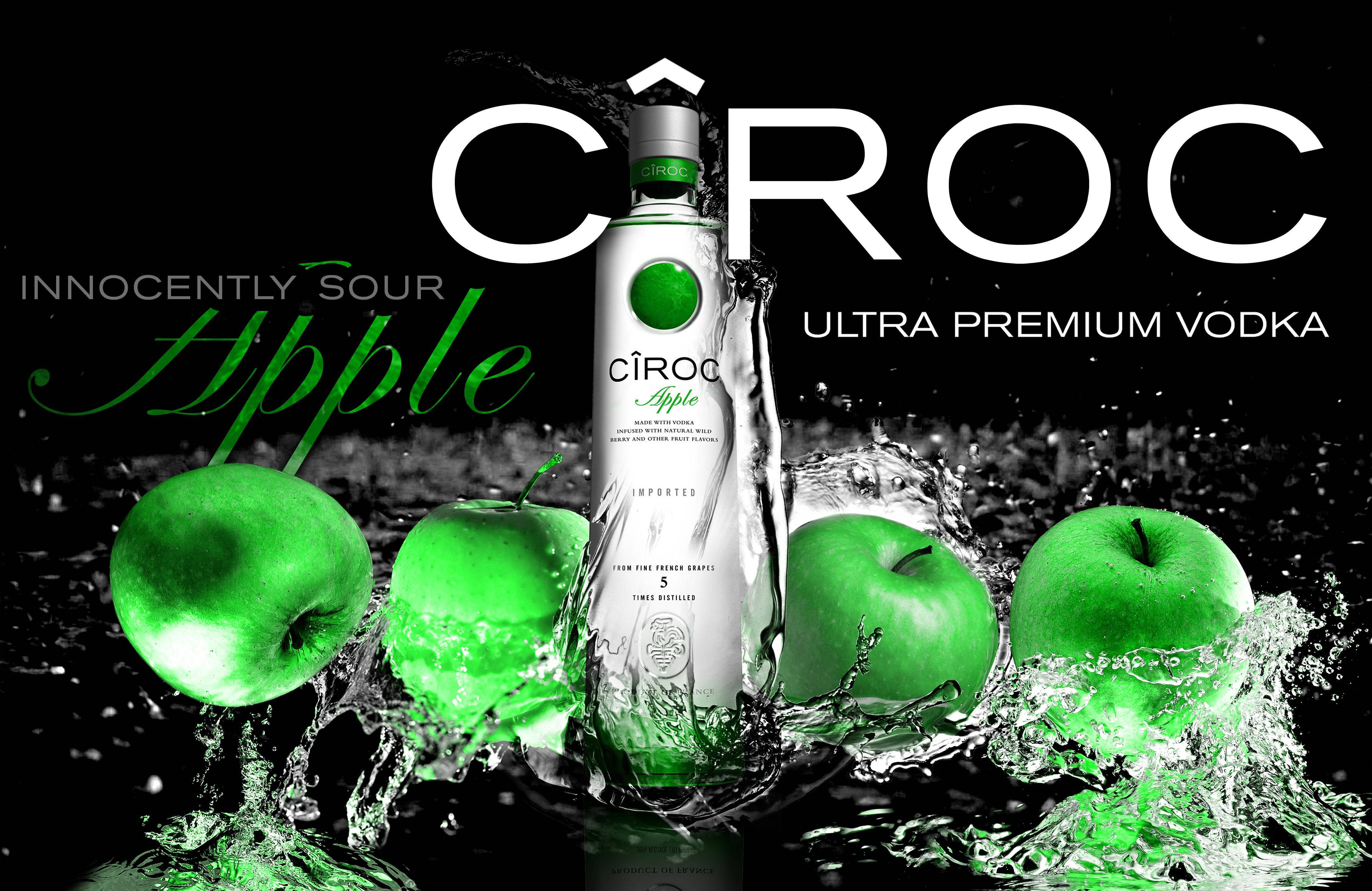 Ciroc 超級高級法國伏特加蘋果口味 壁紙 — 在黑色背景下，一瓶時尚的Ciroc Apple伏特加被鮮綠色的蘋果和飛濺的水花環繞。